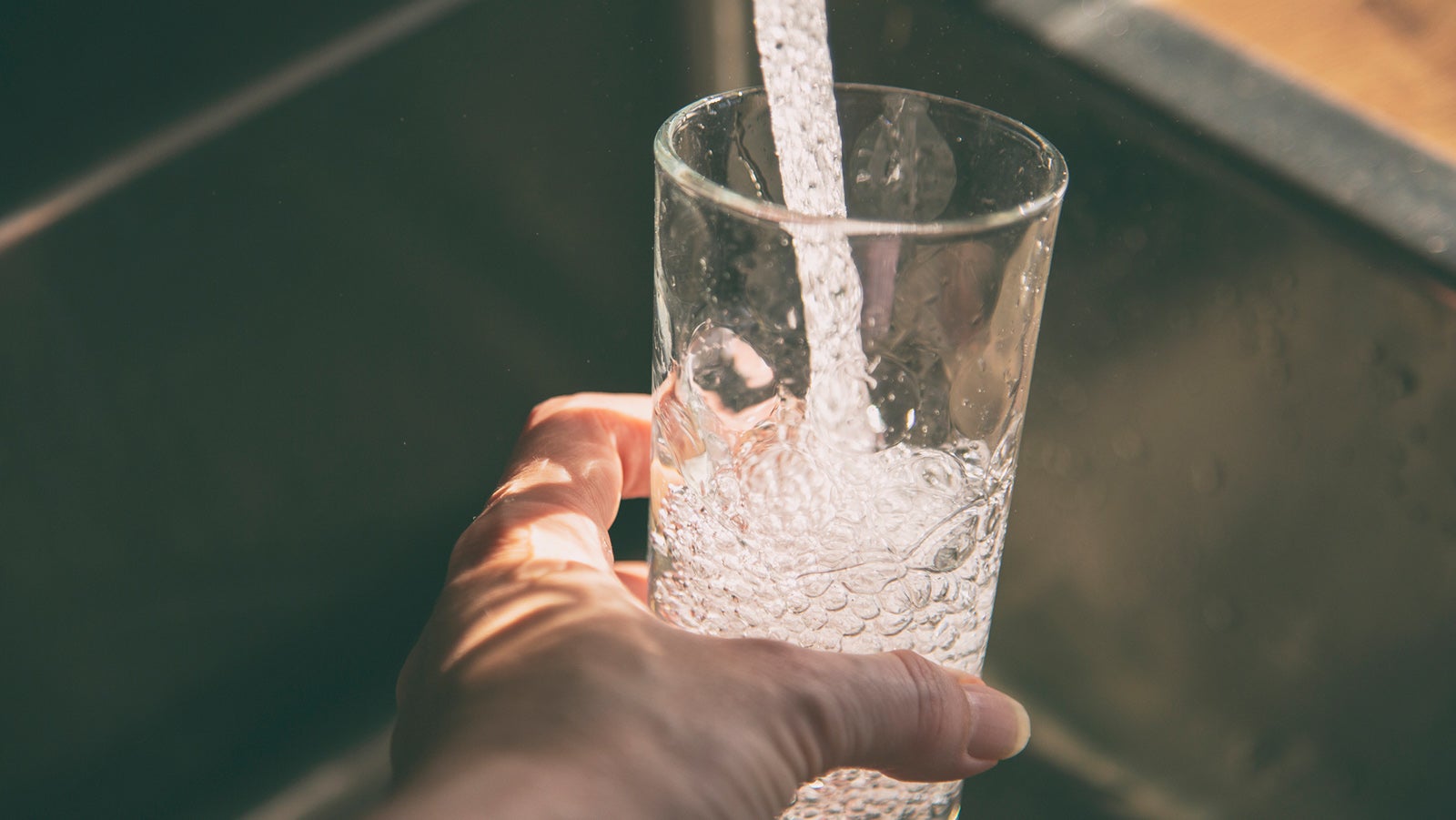 Female pouring fresh drinking tap water into the glass. Close-up on hand holding glass.
