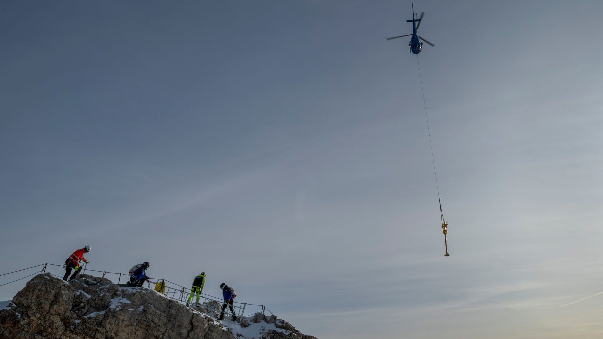 11.11.2025, Bayern, Garmisch-Partenkirchen: Das Zugspitz-Gipfelkreuz wird mit einem Helikopter ins Tal geflogen, um dort von einem Kunstschmiede-Betrieb restauriert zu werden. (Peter Kneffel/dpa)