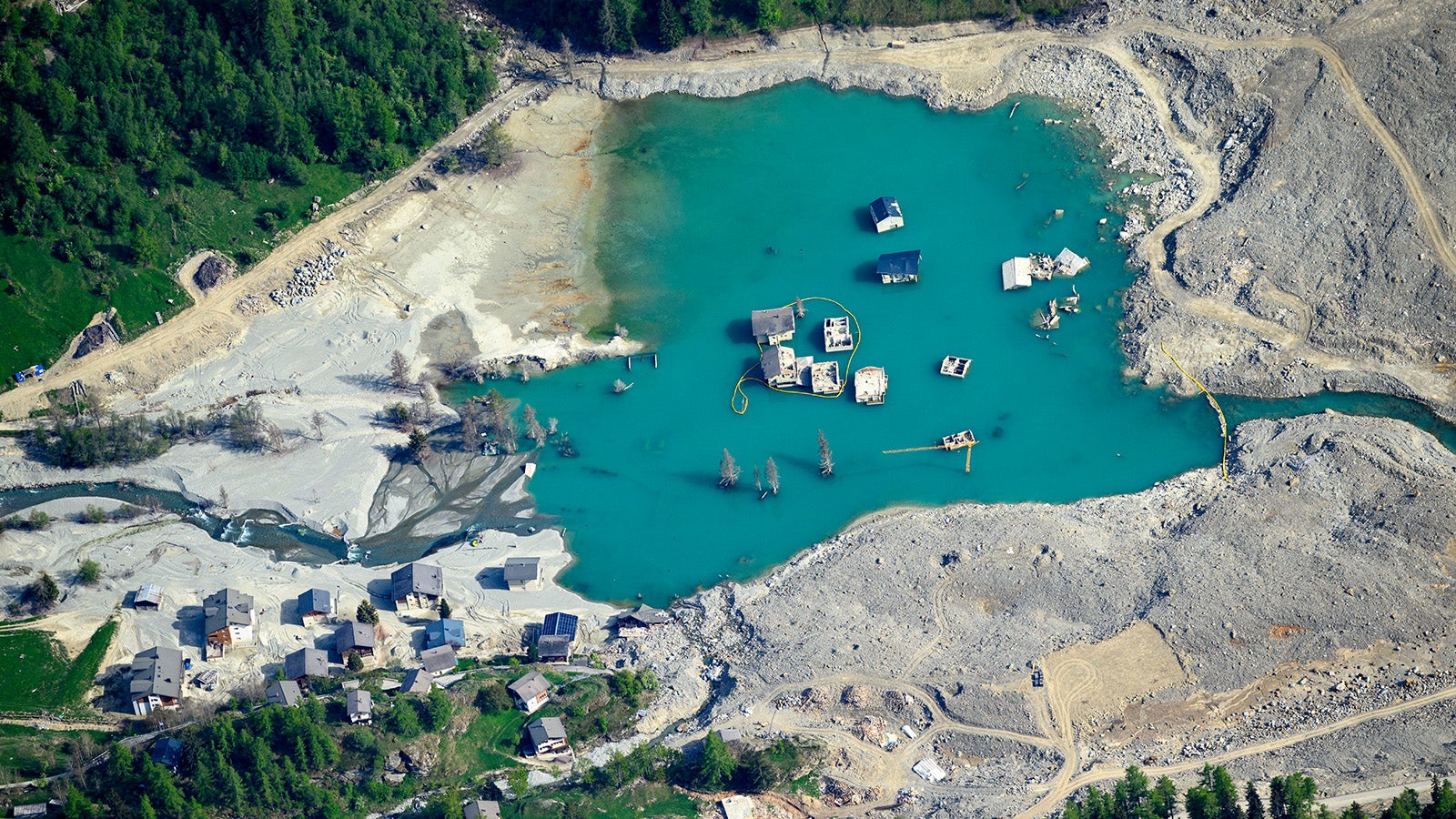 ARCHIV - 21.05.2026, Schweiz, Blatten: Der Felssturz mit den Tr&uuml;mmern und dem dadurch aus dem Fluss Lonza entstandenen See, aus dem versch&uuml;ttete Geb&auml;ude des Dorfes ragen, ist ein Jahr nach dem Felssturz zu sehen. Das Bergdorf Blatten im L&ouml;tschental wurde unter riesigen Ger&ouml;ll- und Eismassen begraben.  (zu dpa: &laquo;Verheerende Sturzflut - Welche Risiken bergen die Alpen?&raquo;) Foto: Laurent Gillieron/KEYSTONE/dpa +++ dpa-Bildfunk +++