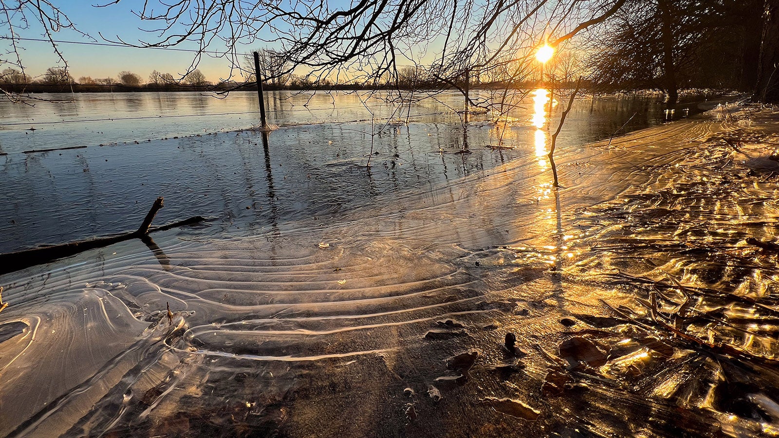 09.01.2024, Niedersachsen, Laatzen: Die Sonne geht in der beim Hochwasser &uuml;berfluteten Leinemasch s&uuml;dlich von Hannover unter. Temperaturen deutlich unter dem Gefrierpunkt verwandeln die &uuml;berfluteten Wiesen und Felder derzeit zu riesige Eisfl&auml;chen. Foto: Julian Stratenschulte/dpa +++ dpa-Bildfunk +++