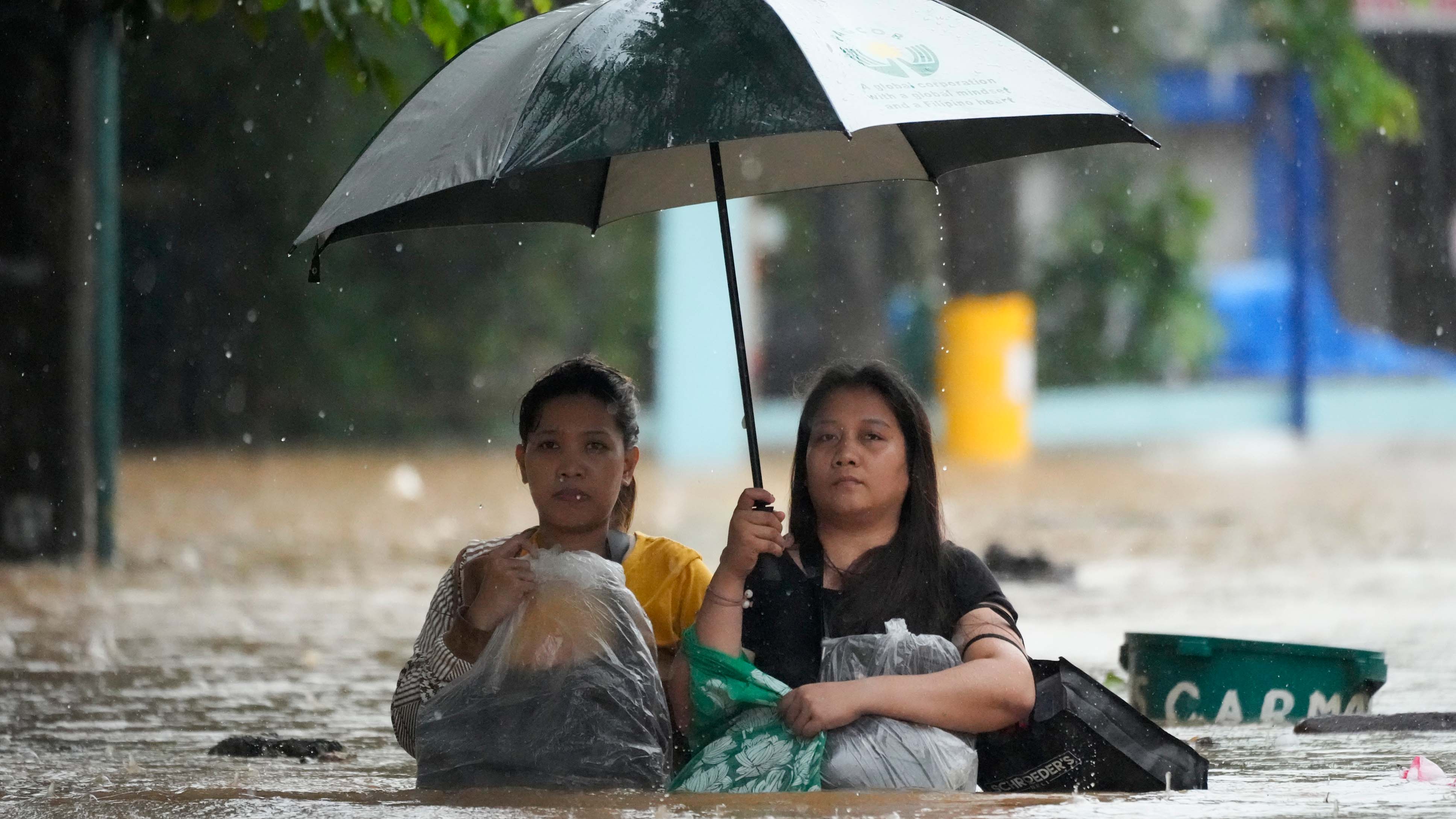 Anwohner sch&uuml;tzen ihr Hab und Gut, w&auml;hrend sie sich durch eine &uuml;berflutete Stra&szlig;e k&auml;mpfen.