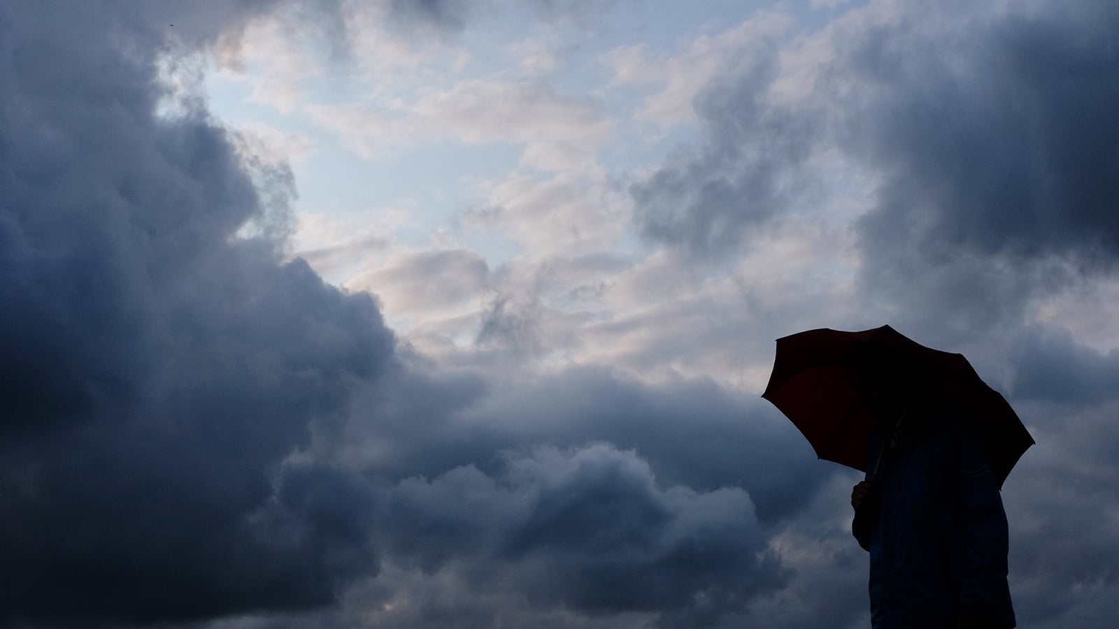 ARCHIV - 12.07.2019, Nordrhein-Westfalen, Duisburg: Ein Mann geht mit einem Regenschirm vor aufziehenden dunklen Wolken spazieren. (zu dpa: &laquo;Saarland im Oktober das w&auml;rmste und nasseste Bundesland&raquo;) Foto: Martin Gerten/dpa +++ dpa-Bildfunk +++