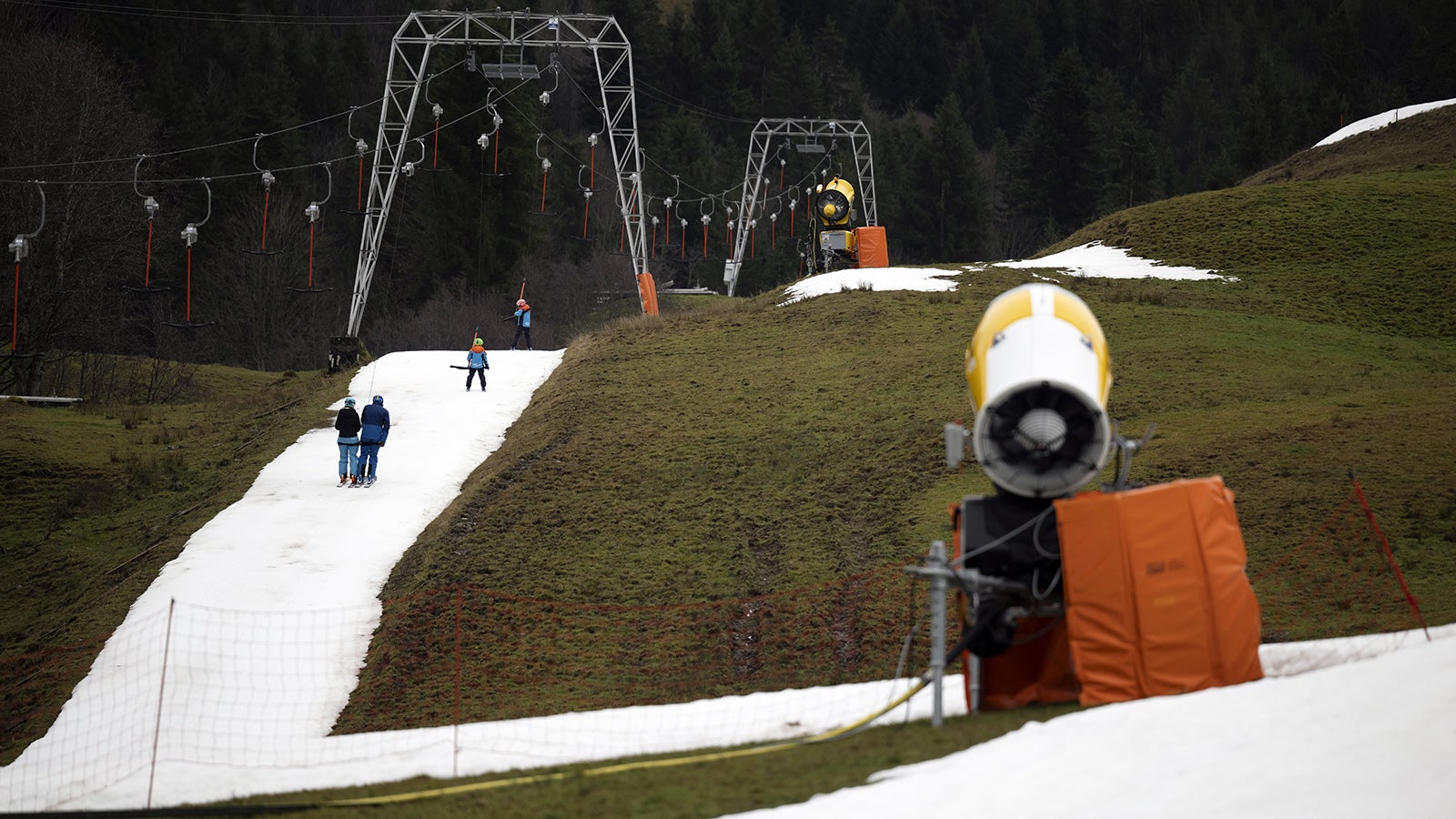 30.12.2022, Schweiz, Schwarzsee: Skifahrer benutzen einen Lift auf einer k&uuml;nstlich beschneiten Piste inmitten eines schneefreien Feldes zwischen dem Gipfel des Lifts und der Schwarzsee Gypsera. Foto: Anthony Anex/KEYSTONE/dpa +++ dpa-Bildfunk +++