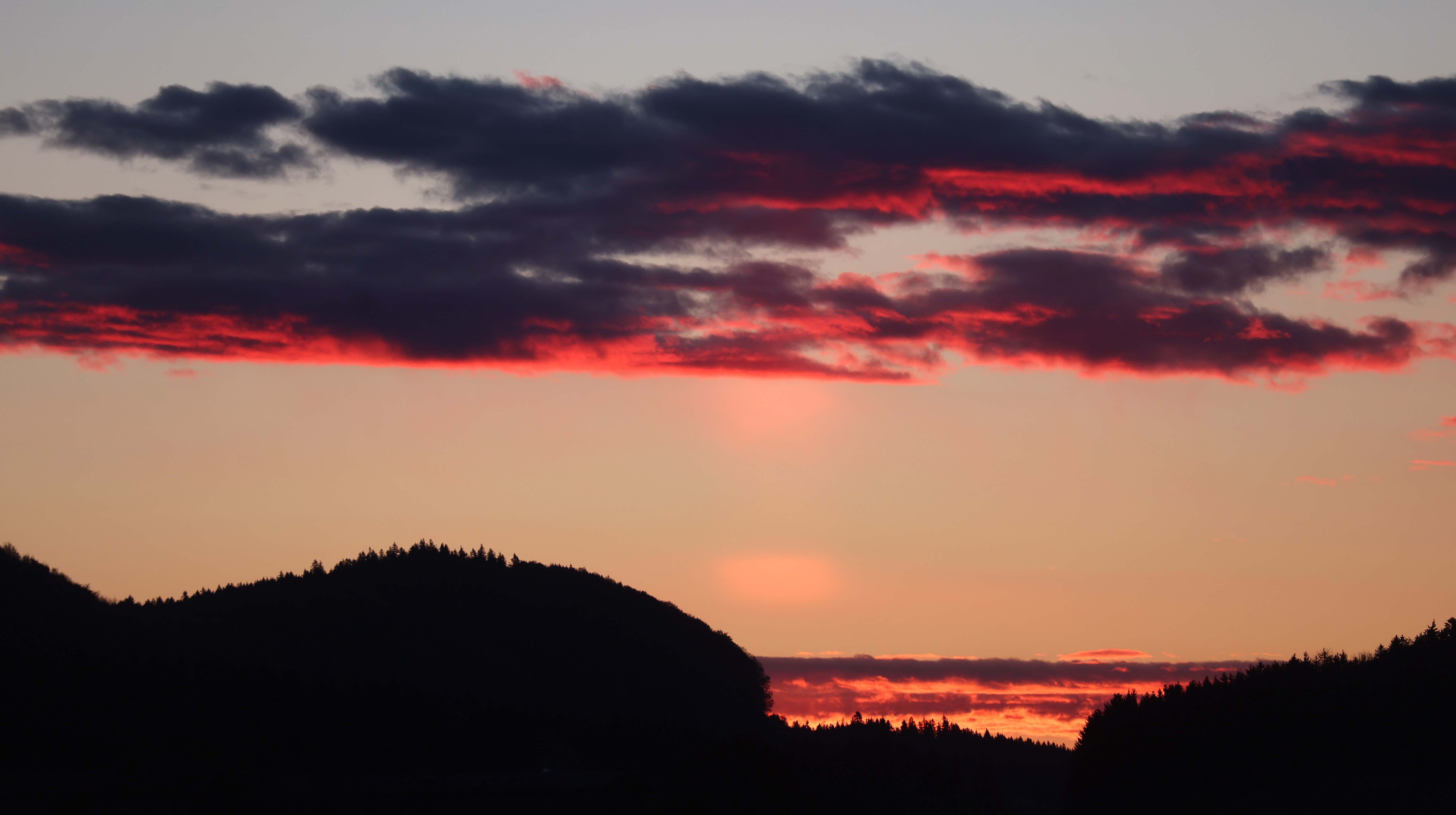 Die aufgehende Sonne f&auml;rbt die Wolken &uuml;ber den Bergen in verschiedene Rott&ouml;ne. 