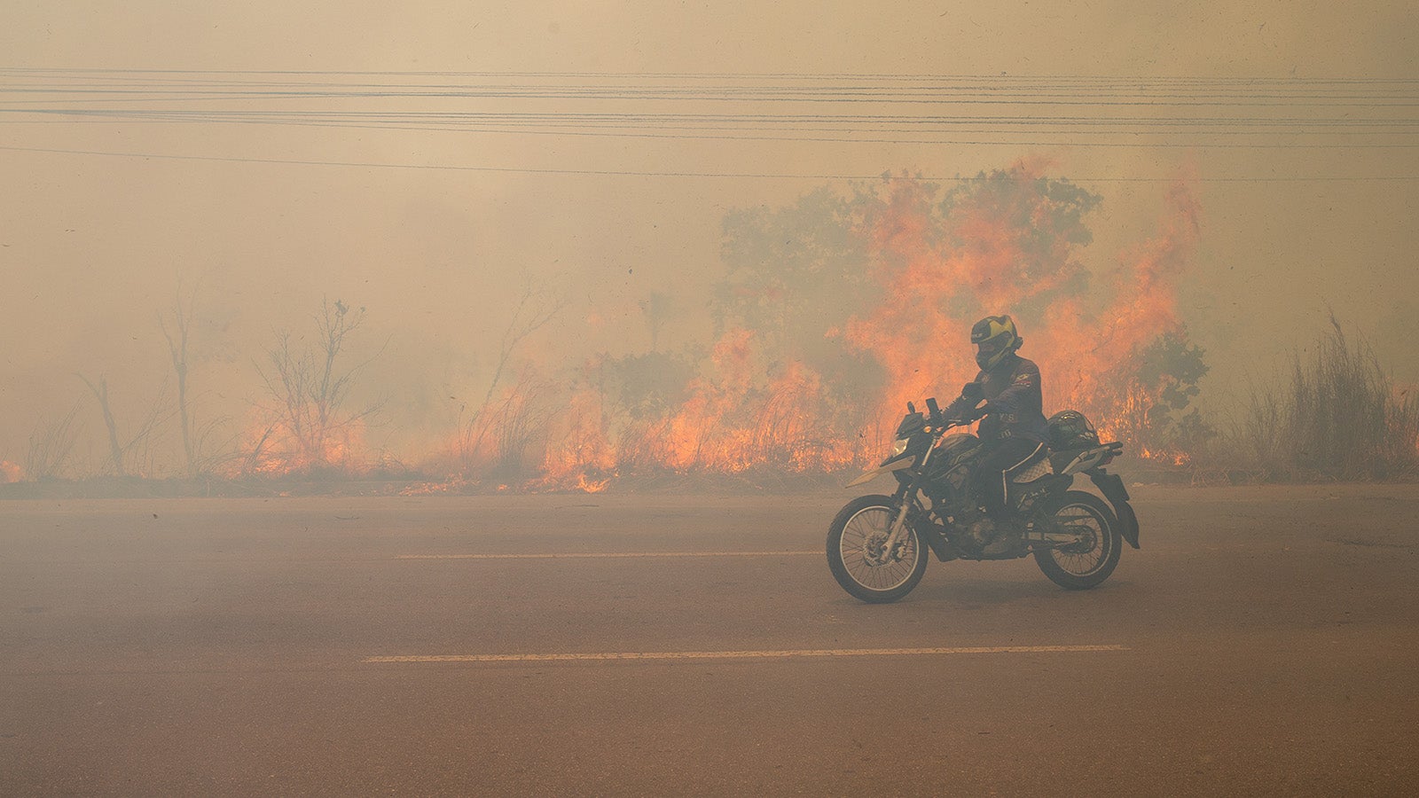 Ein Motorradfahrer f&auml;hrt w&auml;hrend eines Waldbrandes durch eine von Rauch bedeckte Landstra&szlig;e im Bezirk Cacau Pirera in der Gemeinde Iranduba nahe der Stadt Manaus. Auch &uuml;ber der Stadt Manaus lag eine dichte Rauchwolke. Foto: Suamy Beydoun/dpa +++ dpa-Bildfunk +++