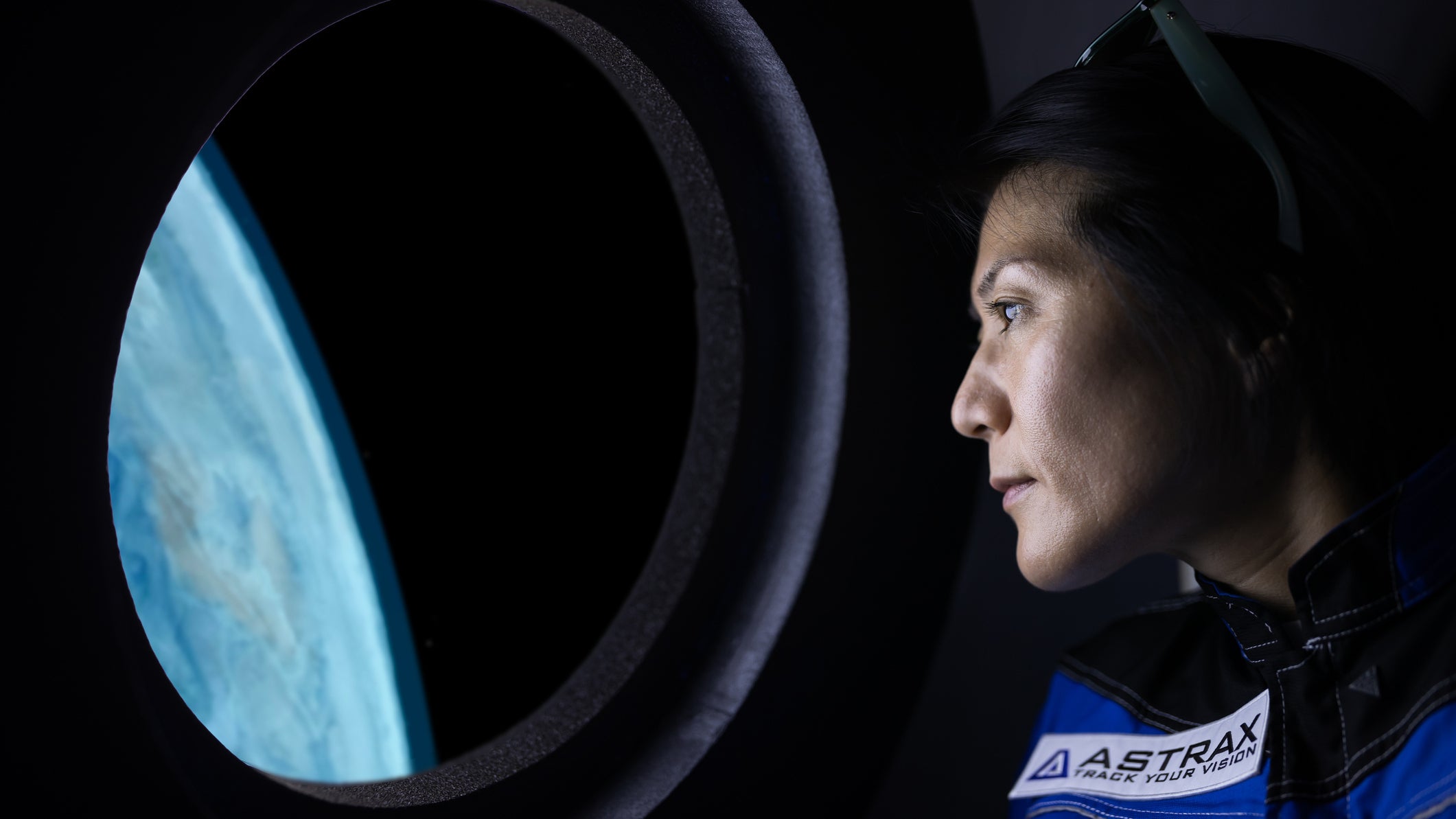 A female commercial space traveler looking at the earth through the window inside of the spaceship.