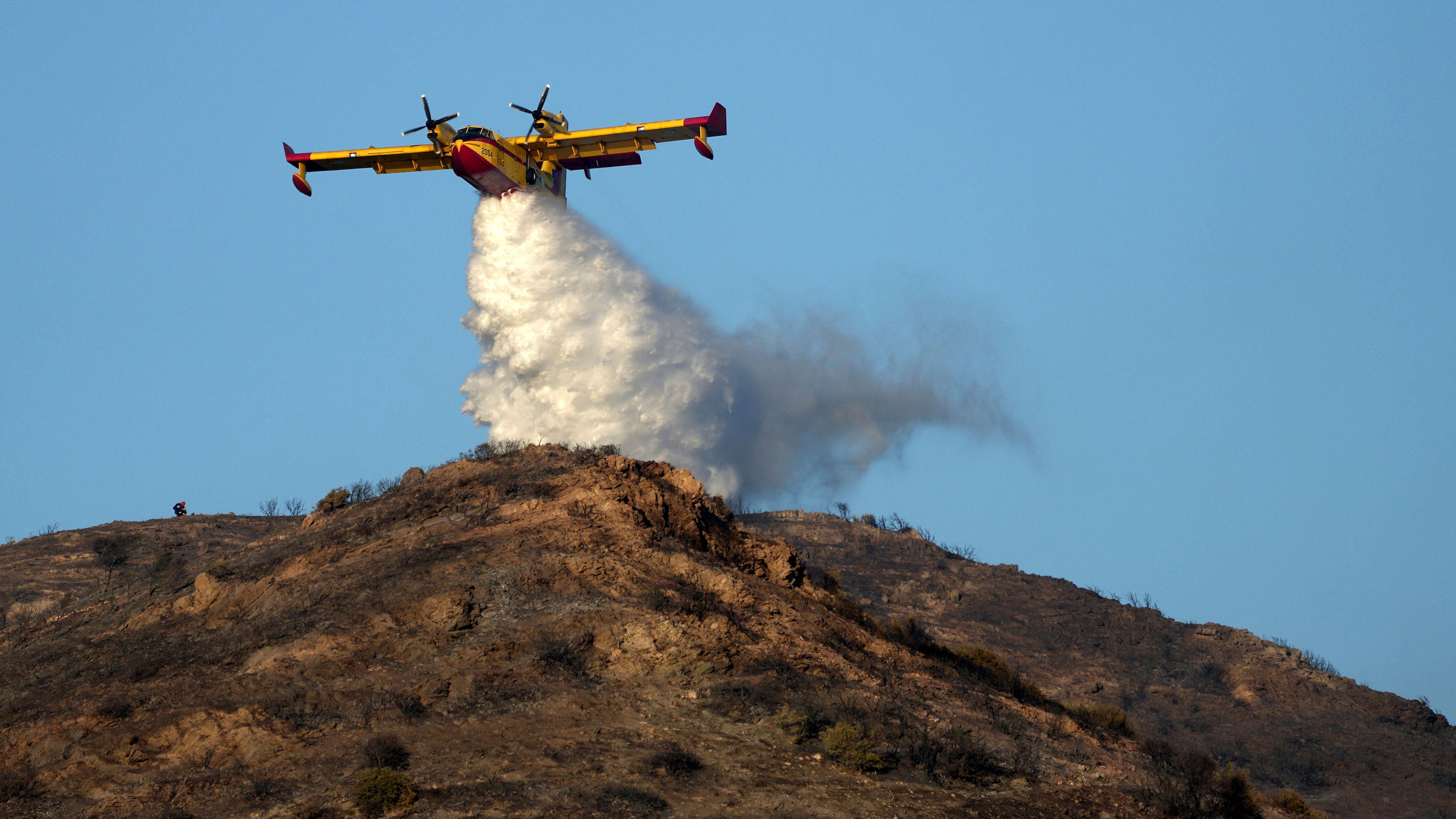 26.06.2025, Griechenland, Athen: Ein L&ouml;schflugzeug verspr&uuml;ht Wasser auf einem H&uuml;gel in Thymari, s&uuml;dlich von Athen. Foto: Thanassis Stavrakis/AP/dpa +++ dpa-Bildfunk +++