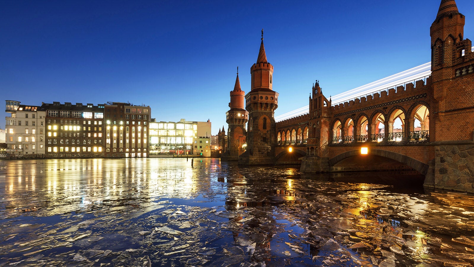 The famous Oberbaubr&uuml;cke in Berlin at Spree River, with ice on the river, blue hour. The "Oberbaum Bridge"  is a double-deck bridge, built 1895, crossing Berlin's River Spree and one of the city's landmarks. It links Friedrichshain and Kreuzberg, and has become an important symbol of Berlin&rsquo;s unity.The lower deck of the bridge carries a roadway, and the upper deck of the bridge carries Berlin subway.