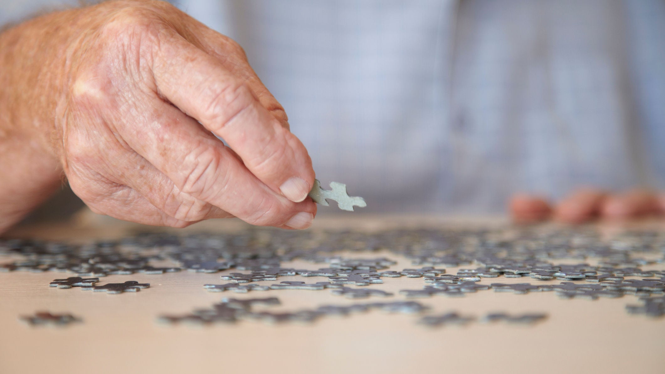 Elderly man, aged 77, looking for pieces of a jigsaw puzzle in a private retirement home