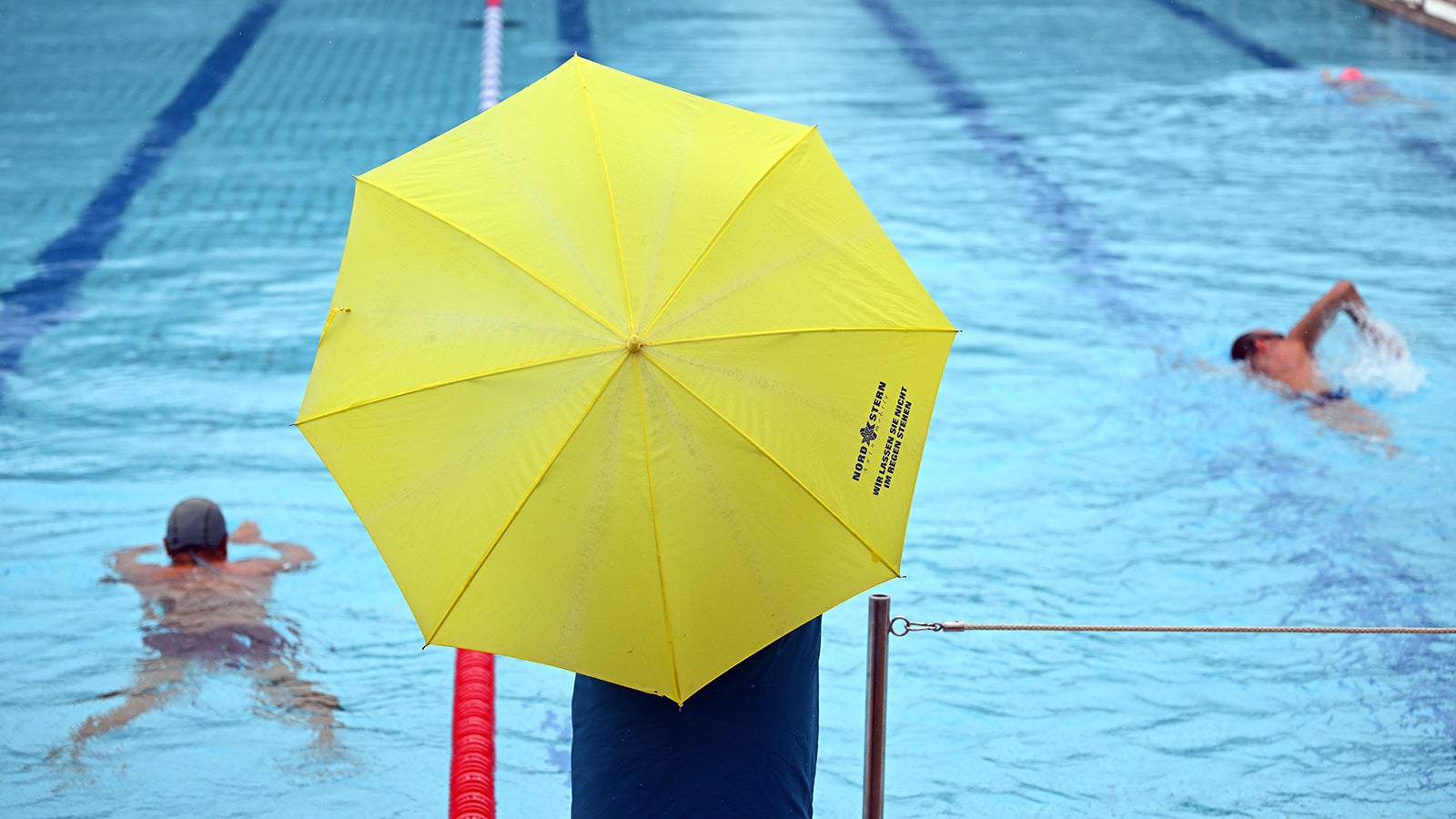 ARCHIV - 07.08.2023, Hessen, Friedrichsdorf Mainz-Kastel: Eine Frau steht bei Regenwetter mit Schirm am Rand des Schwimmerbeckens. (zu dpa: &laquo;Freib&auml;der: Nur die Stammg&auml;ste lassen sich nicht schrecken&raquo;) Foto: Arne Dedert/dpa +++ dpa-Bildfunk +++