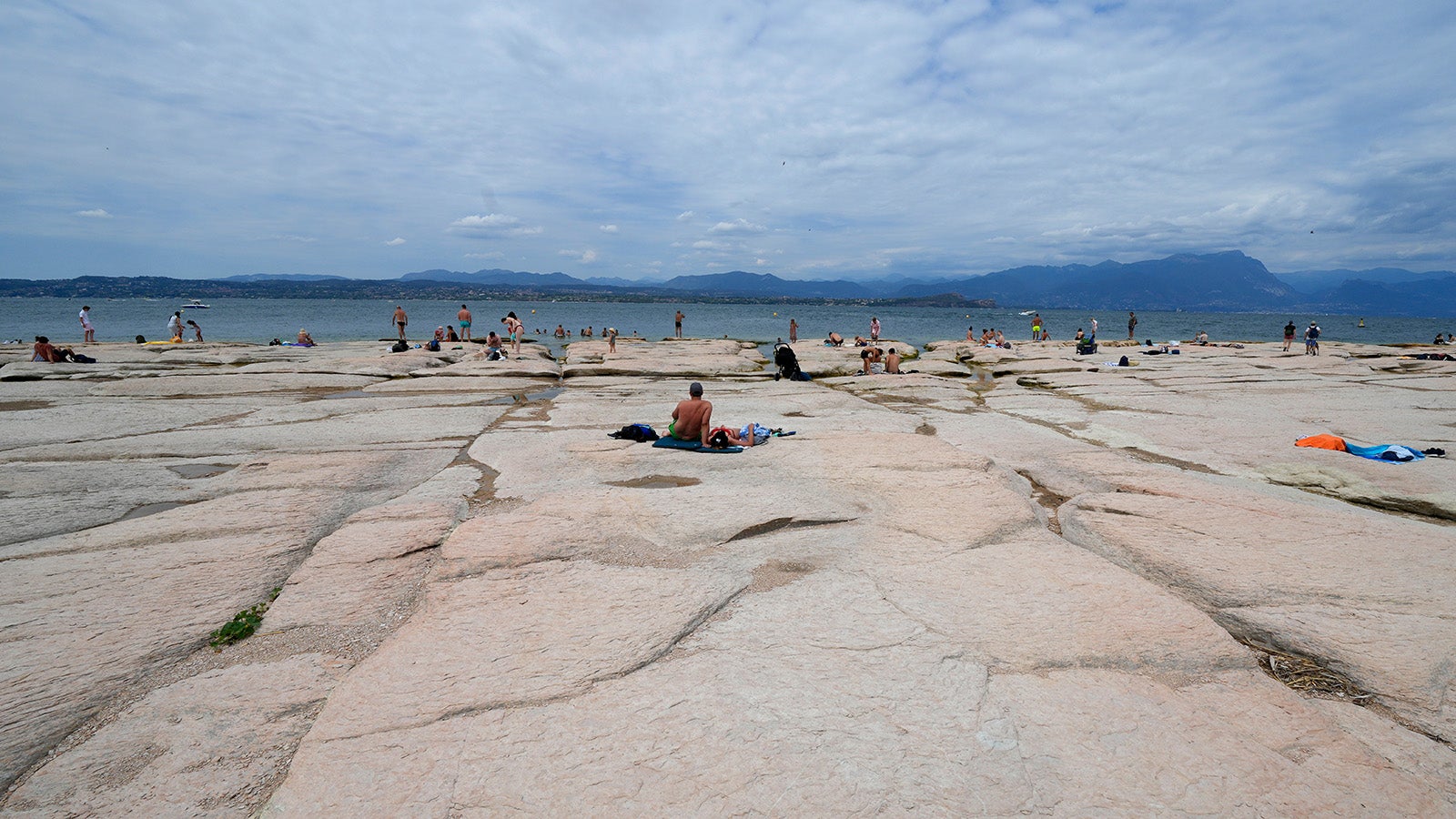 People sunbath on the peninsula of Sirmione, on Garda lake, Italy, Friday, Aug. 12, 2022. Lake Garda water level has dropped critically following severe drought resulting in rocks to emerge around the Sirmione Peninsula. (AP Photo/Antonio Calanni)