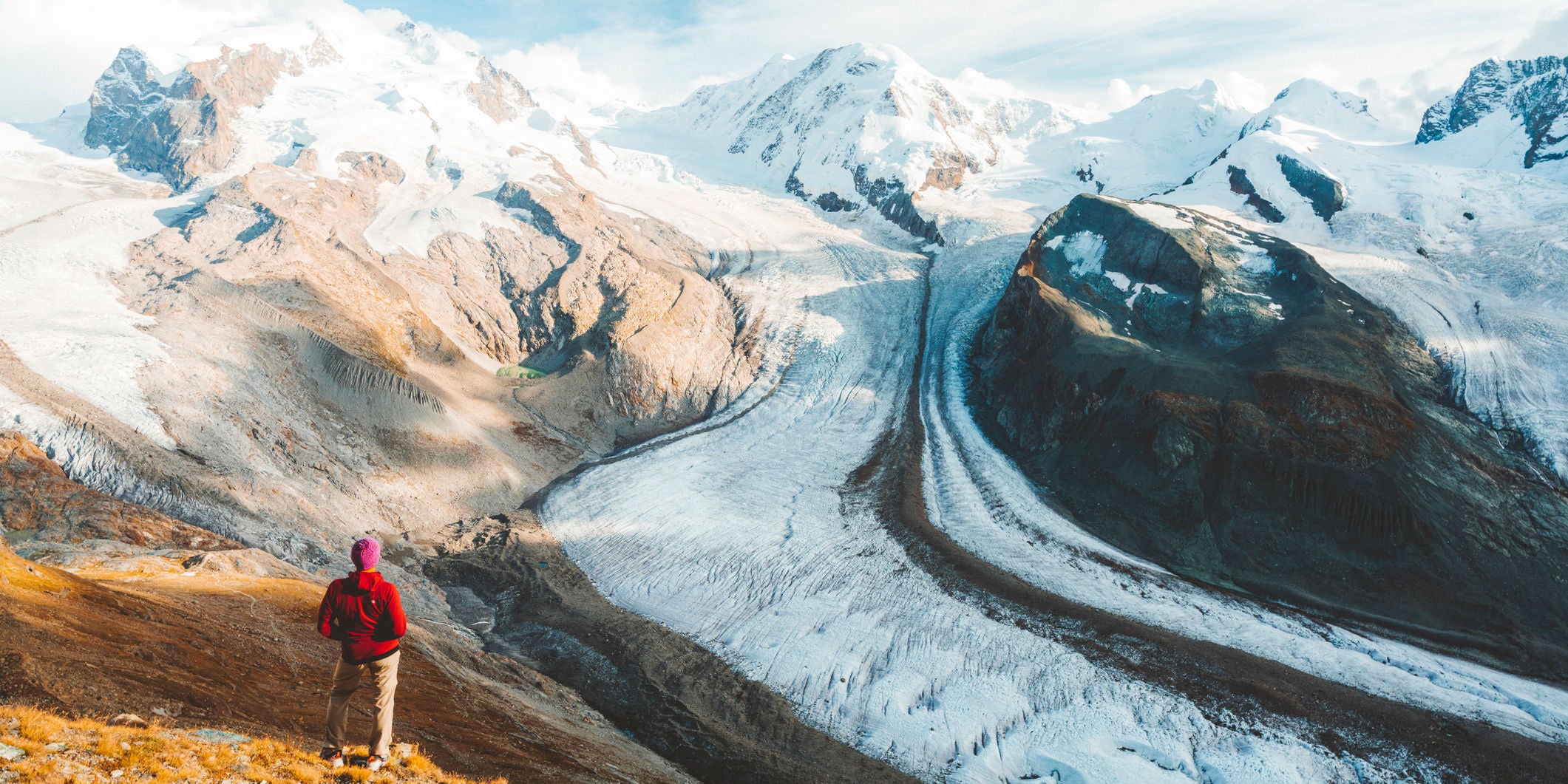 Hiker looking at the snowcapped Lyskamm and Monte Rosa peaks standing above Gorner Glacier, Zermatt, Valais canton, Switzerland