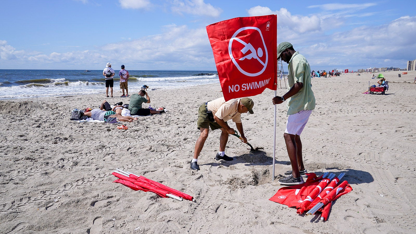 08.08.2023, USA, New York: Mitarbeiter des &laquo;New York City Department of Parks and Recreation&raquo; stellen am Strand von Rockaway eine rote Fahne auf, die Besucher vor einem Badeverbot warnt. Eine 50-j&auml;hrige Frau ist an einem Strand der Millionenmetropole New York von einem Hai schwer verletzt worden. Foto: Mary Altaffer/AP/dpa +++ dpa-Bildfunk +++