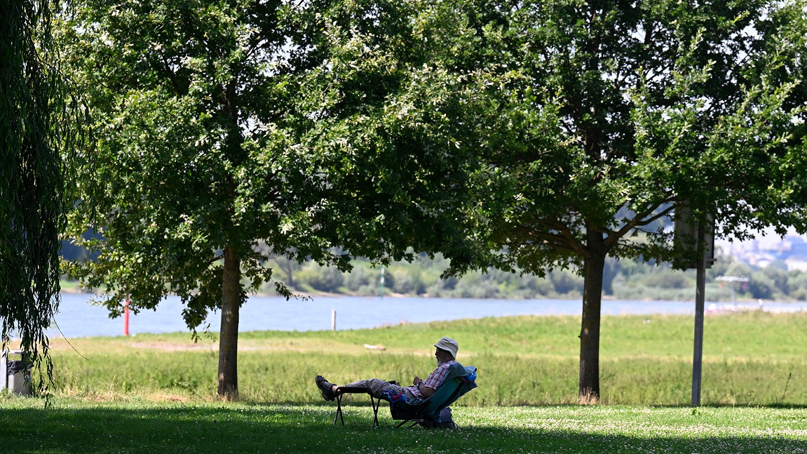 Ein Mann hat sich ein schattiges Pl&auml;tzchen am Ufer des Rheins in Leverkusen gesucht und genie&szlig;t die sommerlichen Temperaturen. Foto: Roberto Pfeil/dpa +++ dpa-Bildfunk +++