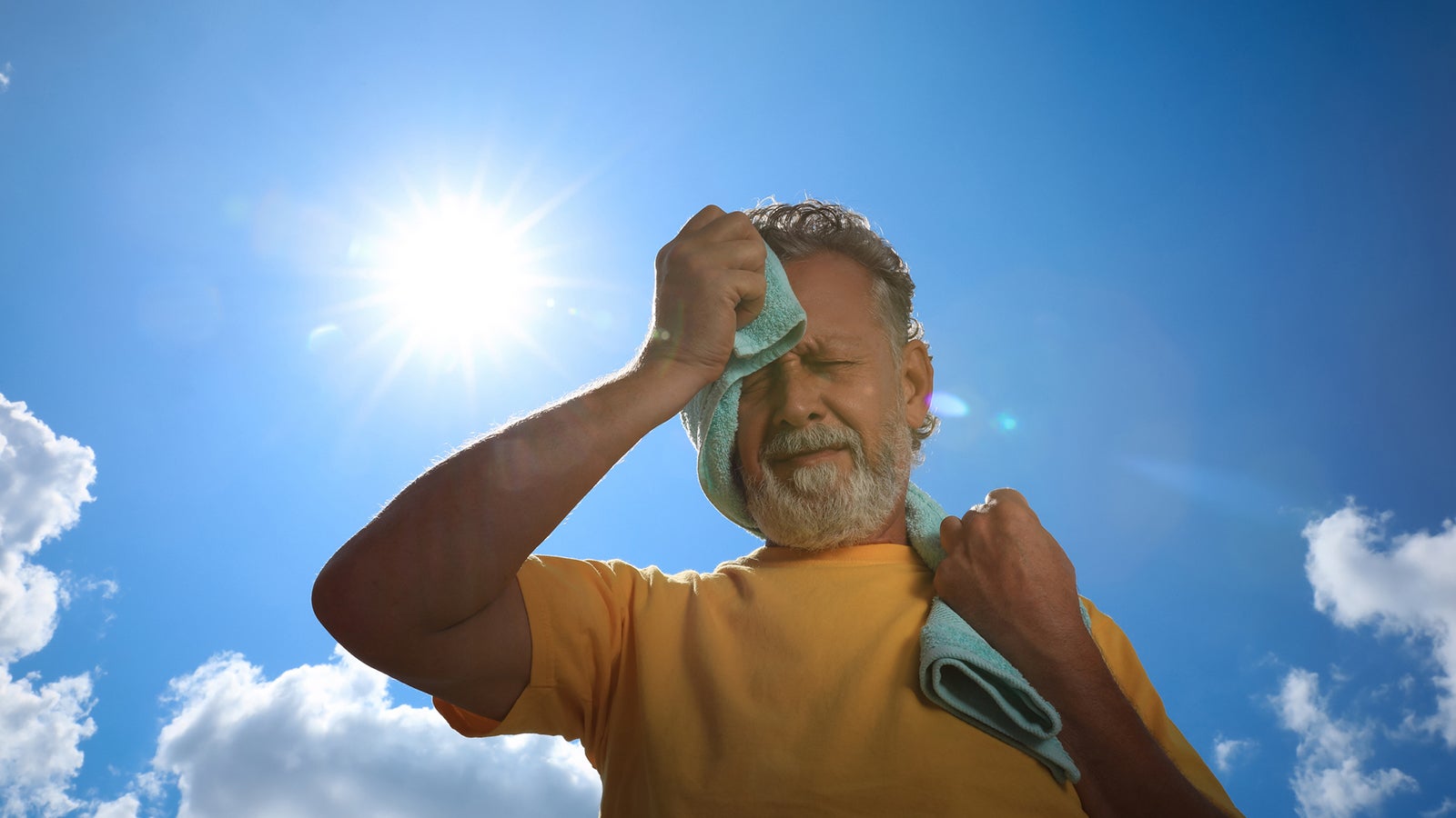 Senior man with towel suffering from heat stroke outdoors, low angle view