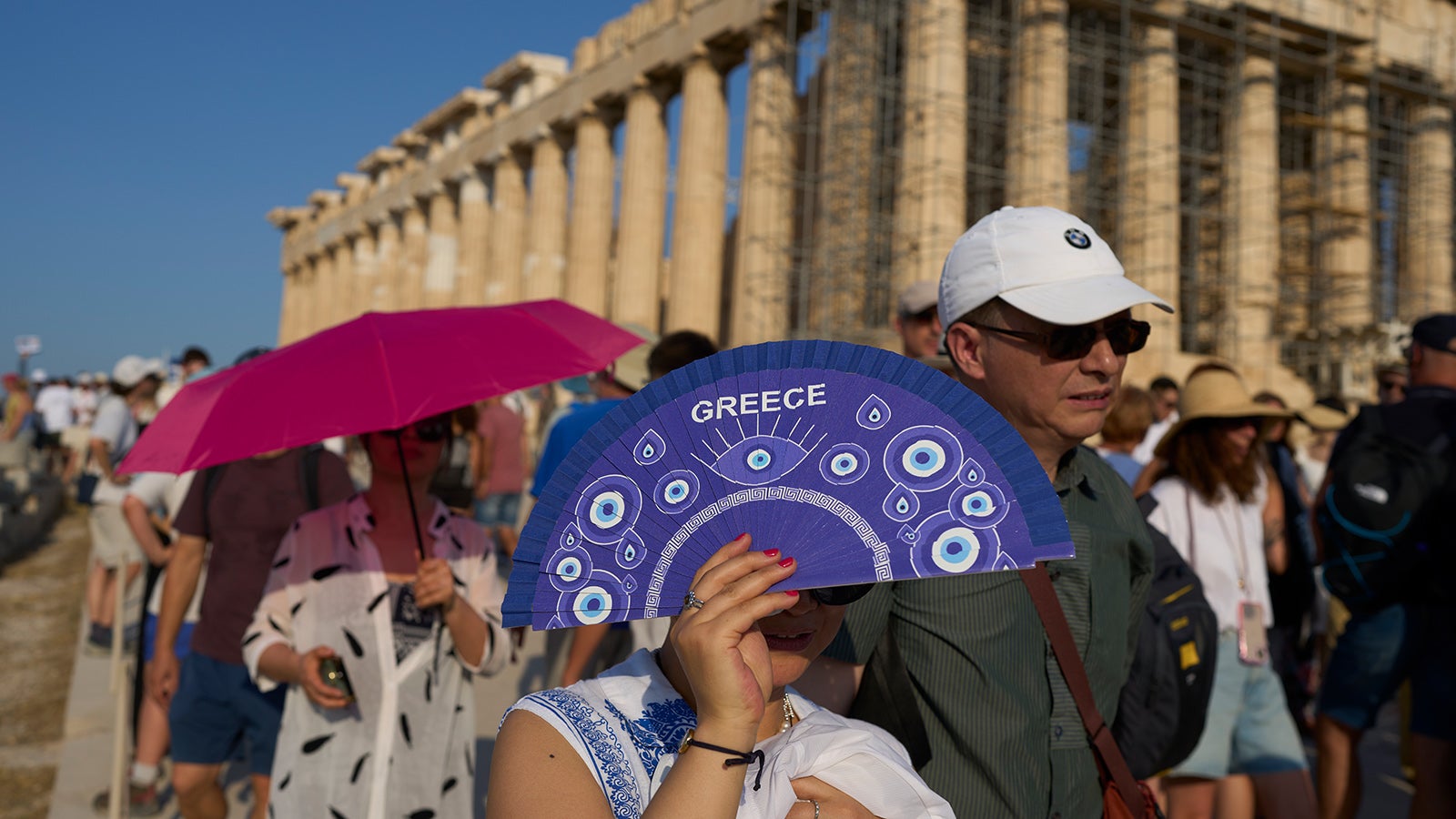 ARCHIV - 25.07.2025, Griechenland, Athen: Touristen benutzen einen F&auml;cher und einen Regenschirm, um sich vor Hitze Sonne zu sch&uuml;tzen, w&auml;hrend sie vor dem Parthenon-Tempel aus dem 5. Jahrhundert v. Chr. auf dem Akropolis-H&uuml;gel spazieren gehen. (zu dpa: &laquo;Hitze: Was Nord- von S&uuml;deurop&auml;ern lernen k&ouml;nnen&raquo;) Foto: Petros Giannakouris/AP/dpa +++ dpa-Bildfunk +++