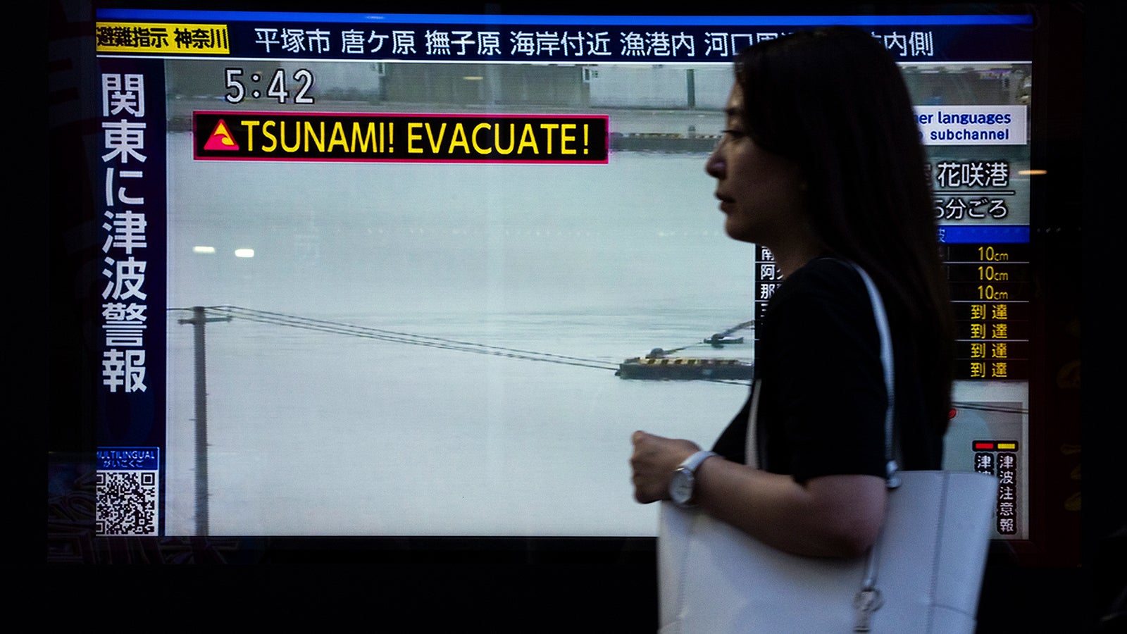 Eine Passantin geht am Mittwoch, dem 30. Juli 2025, in Tokio an einem Fernsehbildschirm vorbei, der eine Tsunami-Warnung zeigt. (AP Photo/Louise Delmotte)
