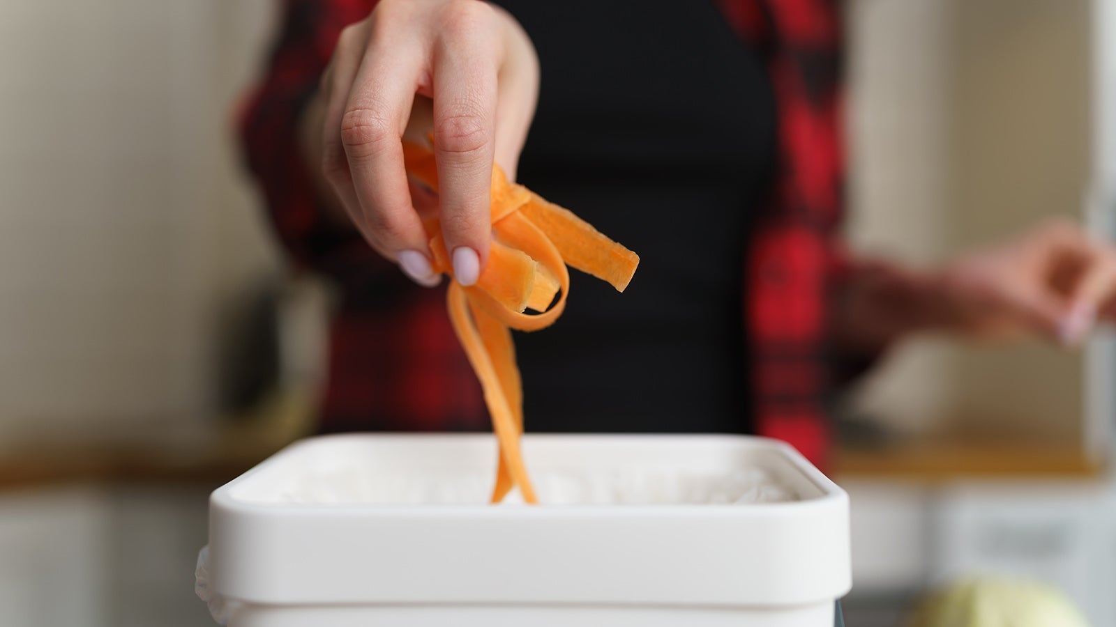 Woman recycling organic food waste in a bokashi bin. Female person throwing vegetable peels into compost container in a domestic kitchen