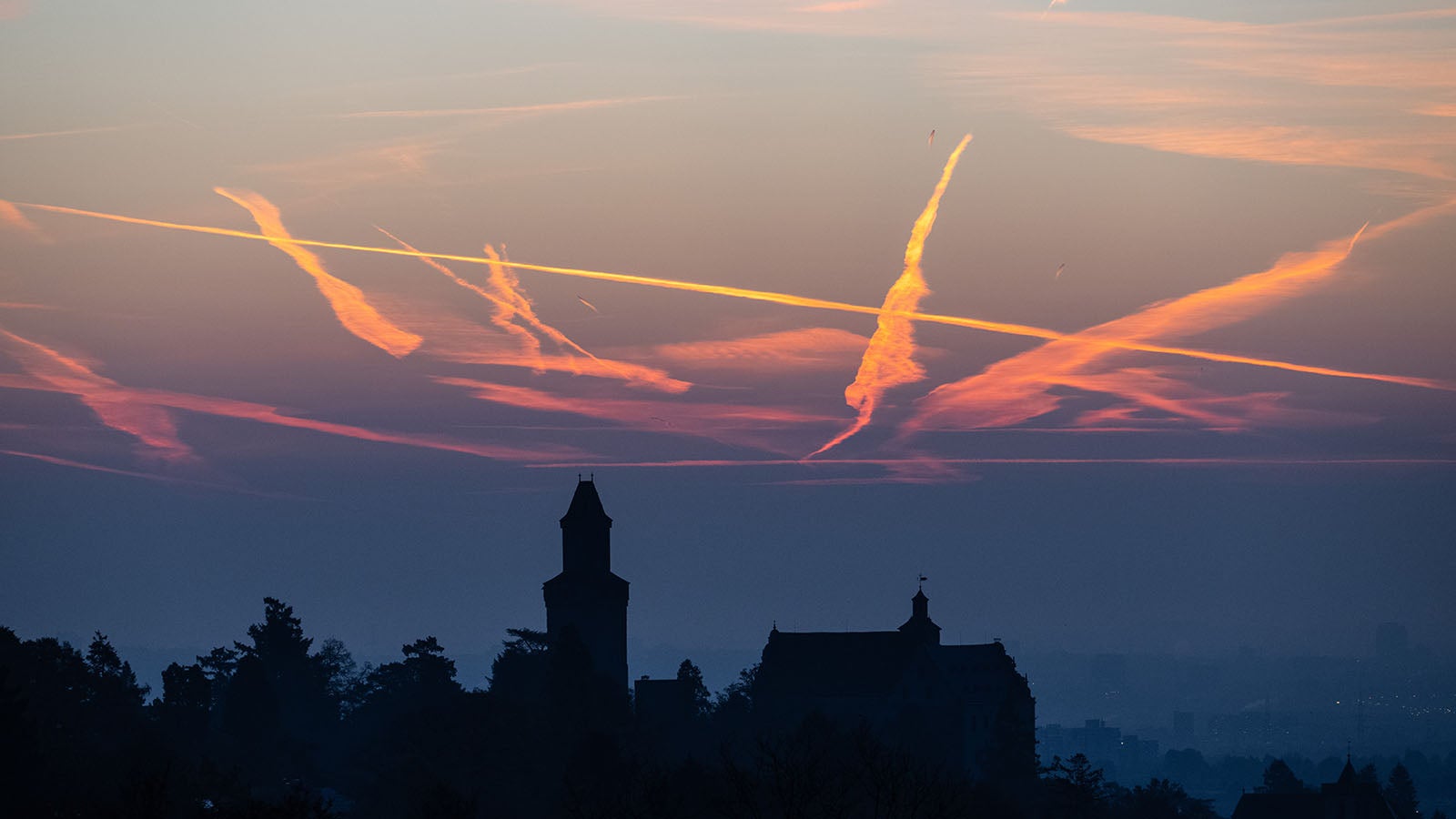 Kurz vor Sonnenaufgang sind die Kondensstreifen vorbeifliegender Flugzeuge &uuml;ber der Burg Kronberg zu sehen. Foto: Boris Roessler/dpa +++ dpa-Bildfunk +++