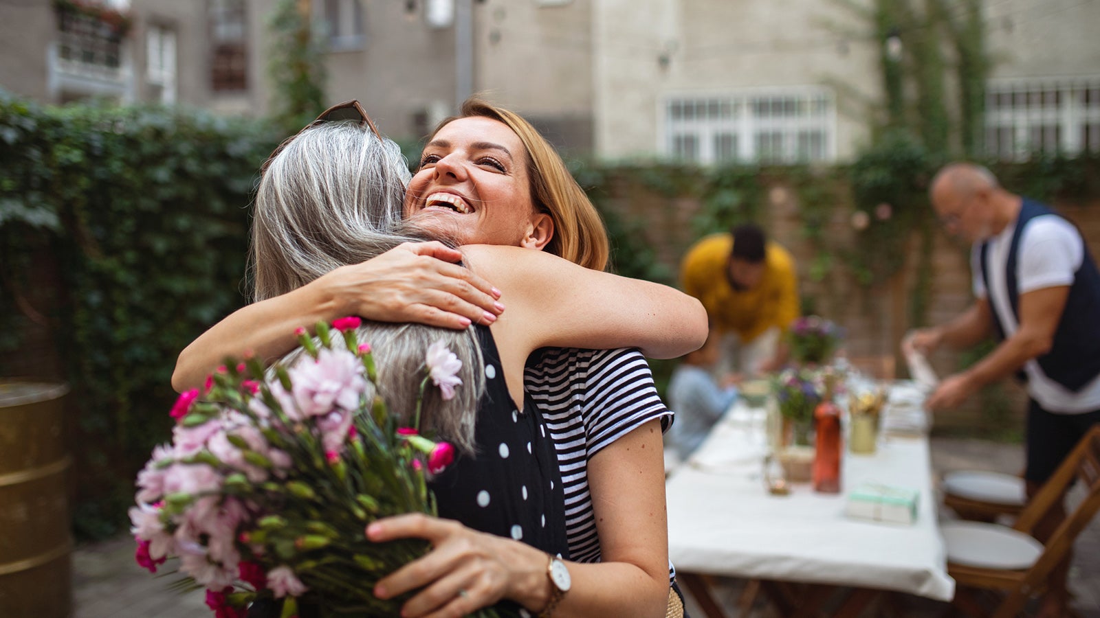 Rear view of senior woman getting flowers from her adult daughter outdoors in front or back yard.