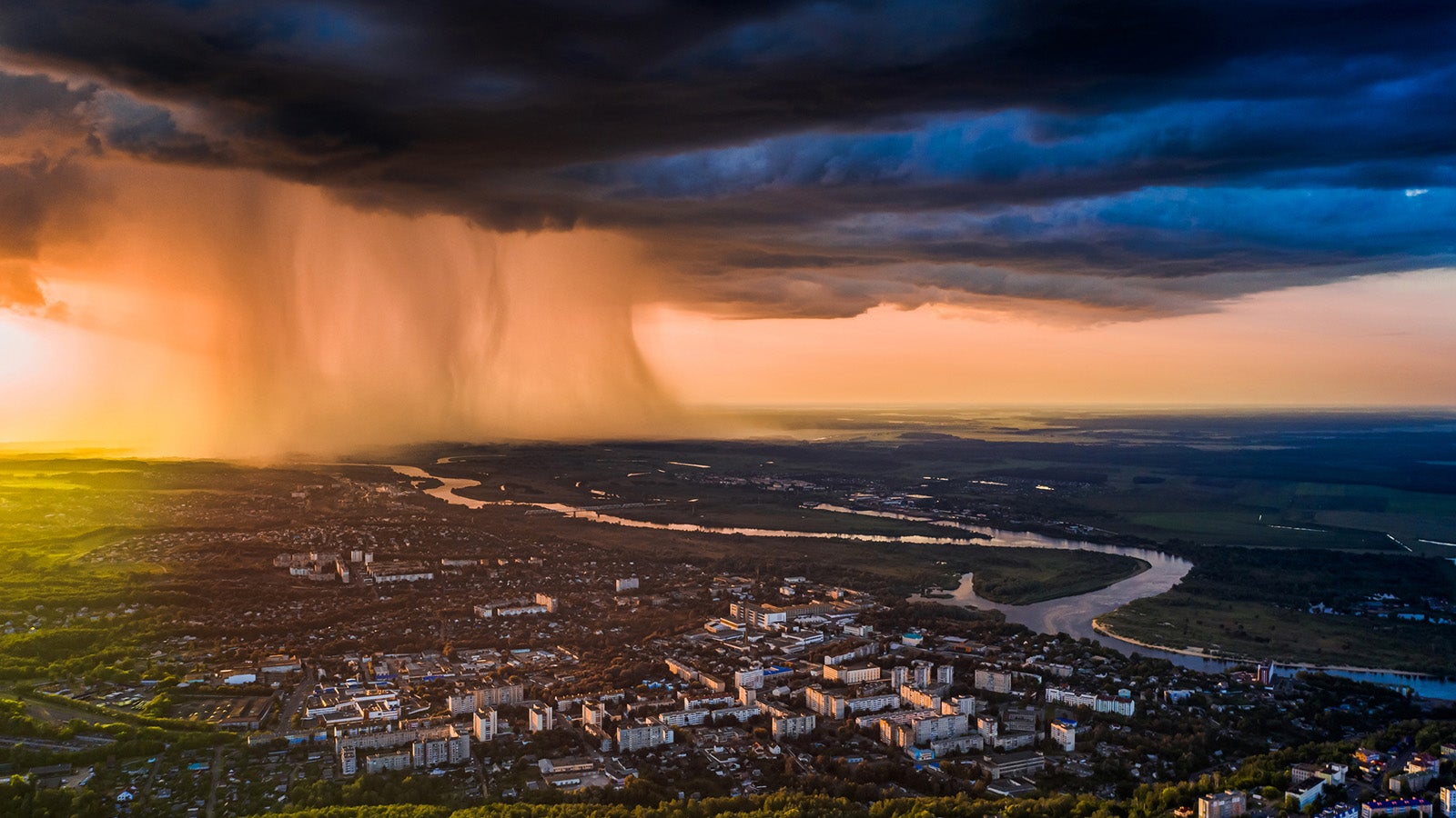 Luftaufnahme einer Stadt mit einem breiten Regenvorhang und dunklen Wolken am Horizont