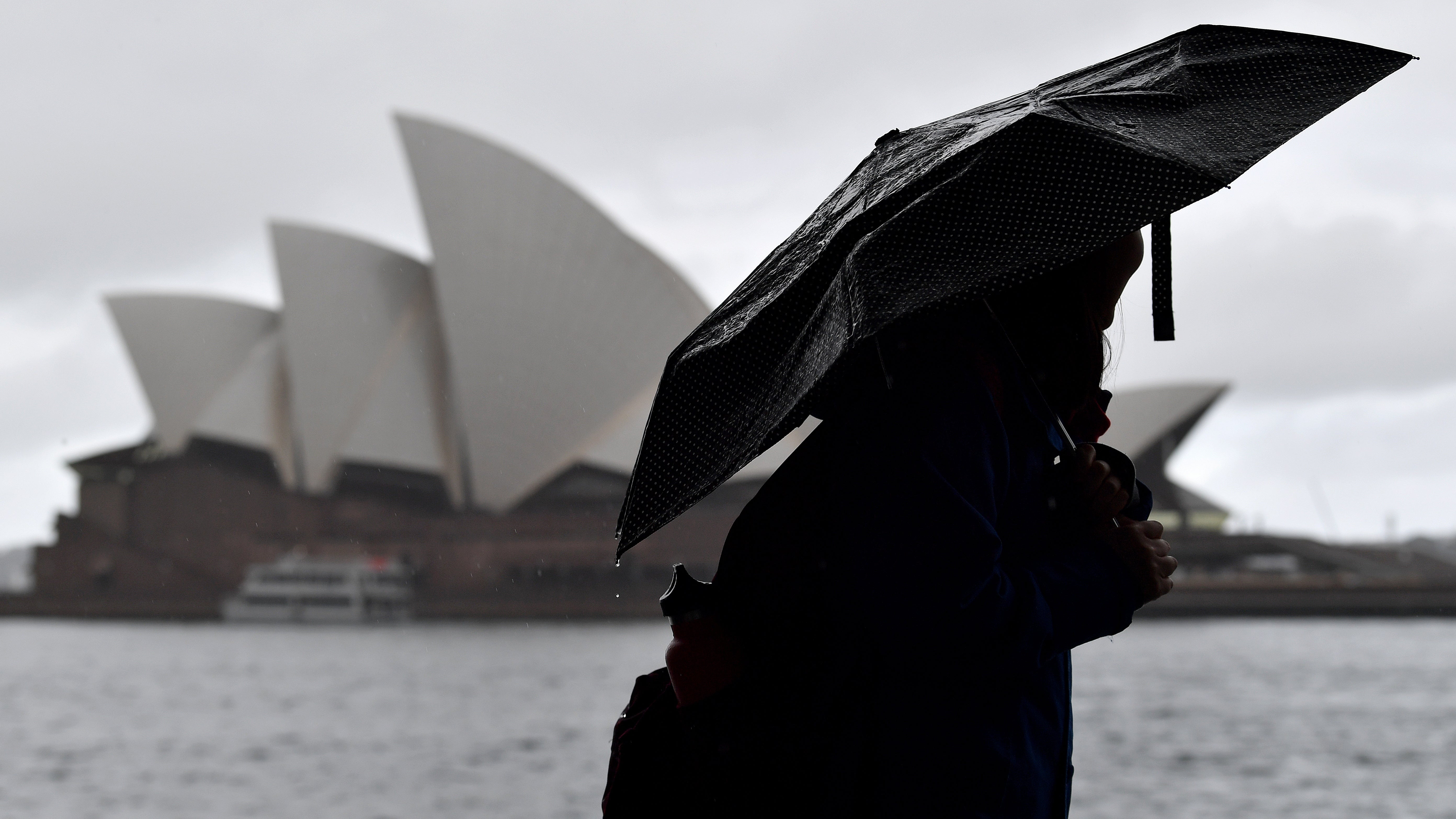Members of the public shelter from the rain under umbrellas as they walk past the Opera House in Sydney, Thursday, October 6, 2022. Hazardous surf and swell are expected on the Macquarie, Hunter, Sydney, Illawarra, Batemans, and Eden coasts on Wednesday, developing into strong, dangerous coastal winds on Thursday. (AAP Image/Bianca De Marchi) NO ARCHIVING