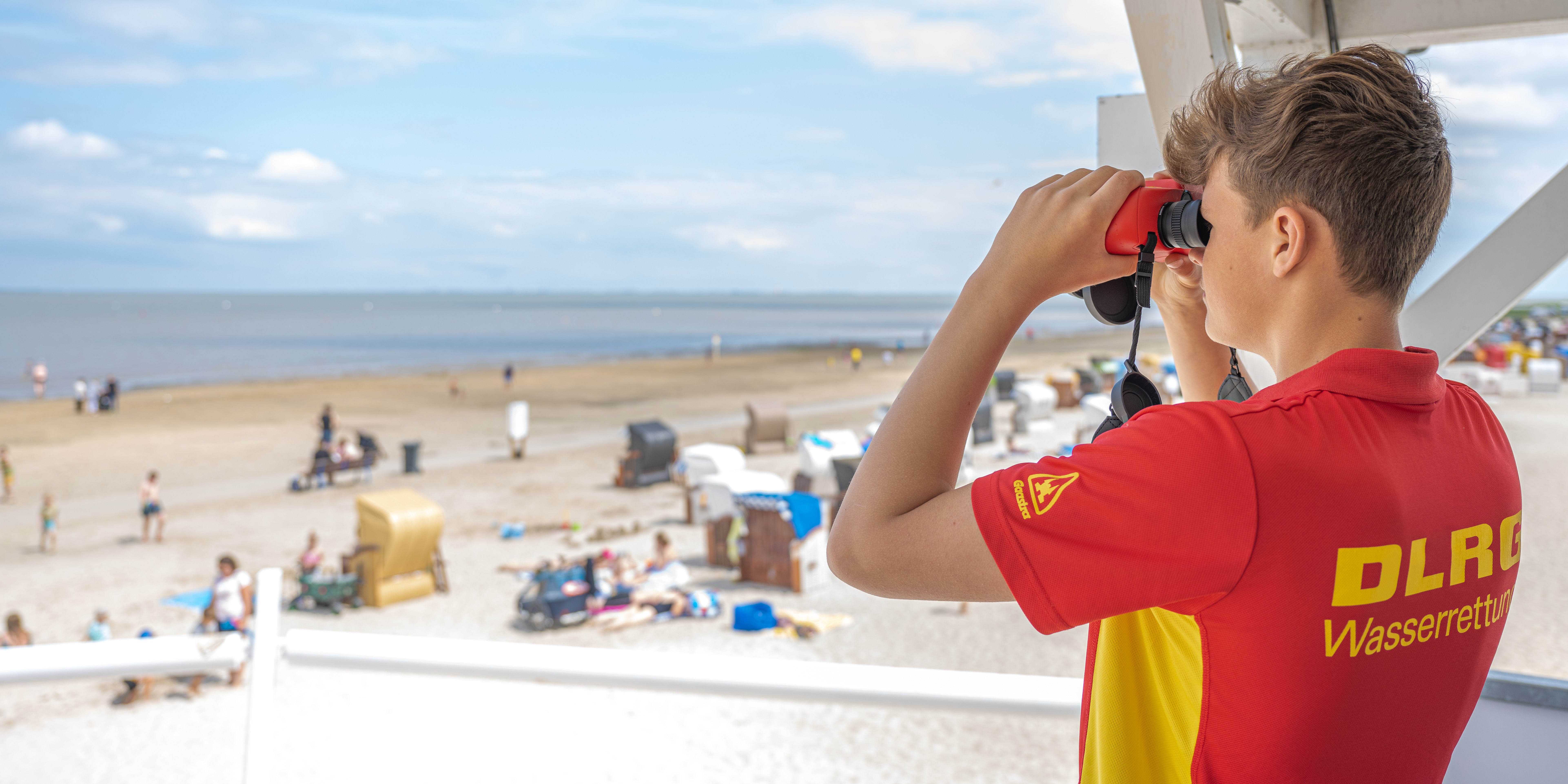 ARCHIV - 26.06.2022, Niedersachsen, Dangast: Peter von der DLRG-Wasserrettung steht auf einem Turm und beaufsichtigt mit einem Fernglas den Badestrand von Dangast. Die DLRG legt die Zahl der Badetoten des vergangenen Jahres vor. (zu dpa: &laquo;DLRG zur Badesaison 2023: Wie viele Menschen sind ertrunken?&raquo;) Foto: Mohssen Assanimoghaddam/dpa +++ dpa-Bildfunk +++