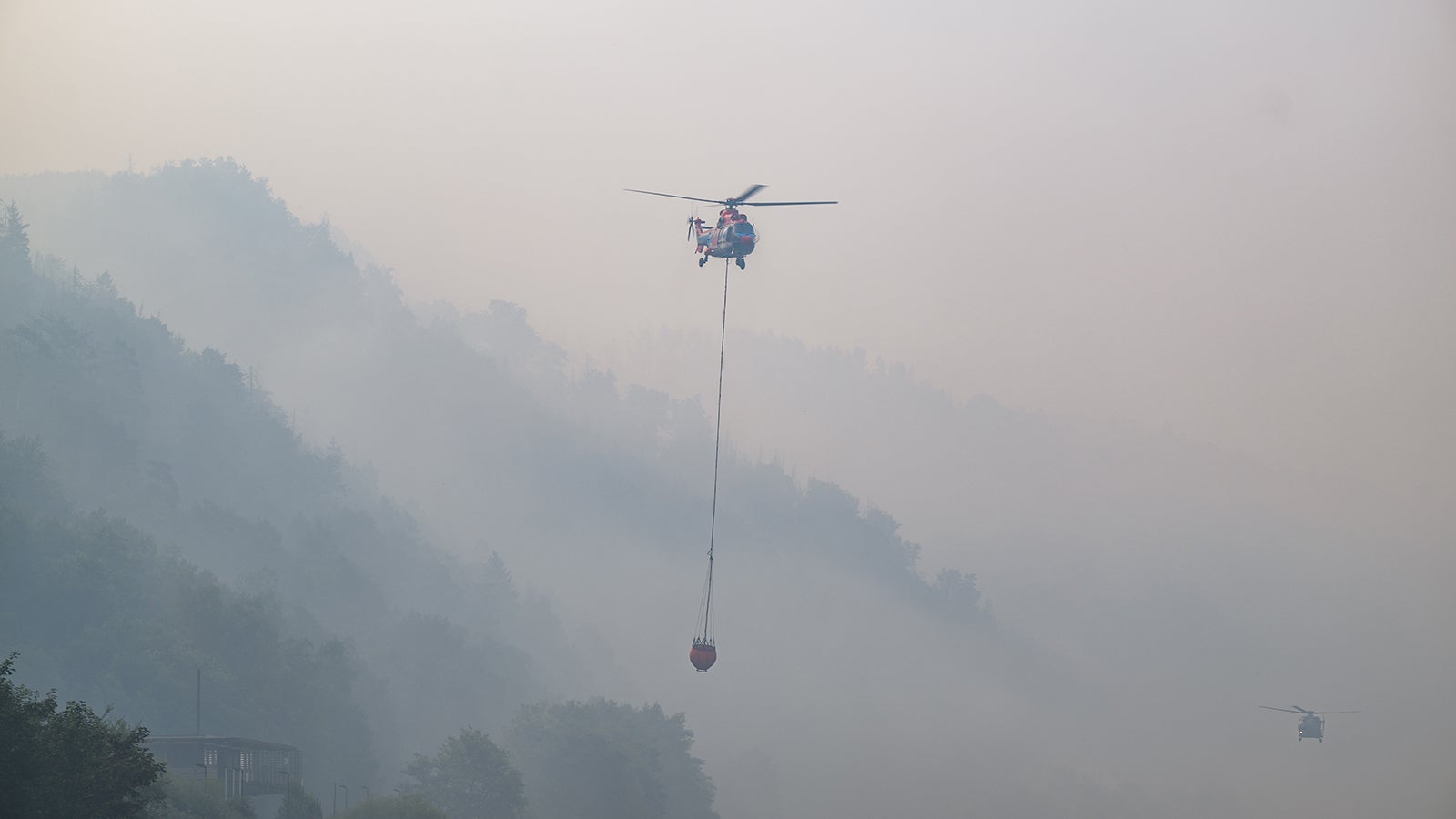 28.07.2022, Sachsen, Schmilka: Ein Lastenhubschrauber aus &Ouml;sterreich nimmt mit einem L&ouml;schwasser-Au&szlig;enlastbeh&auml;lter aus der Elbe Wasser auf um einen Brand im Nationalpark S&auml;chsische Schweiz zu l&ouml;schen. Der Waldbrand im Nationalpark S&auml;chsische Schweiz weitet sich aus. Foto: Robert Michael/dpa +++ dpa-Bildfunk +++