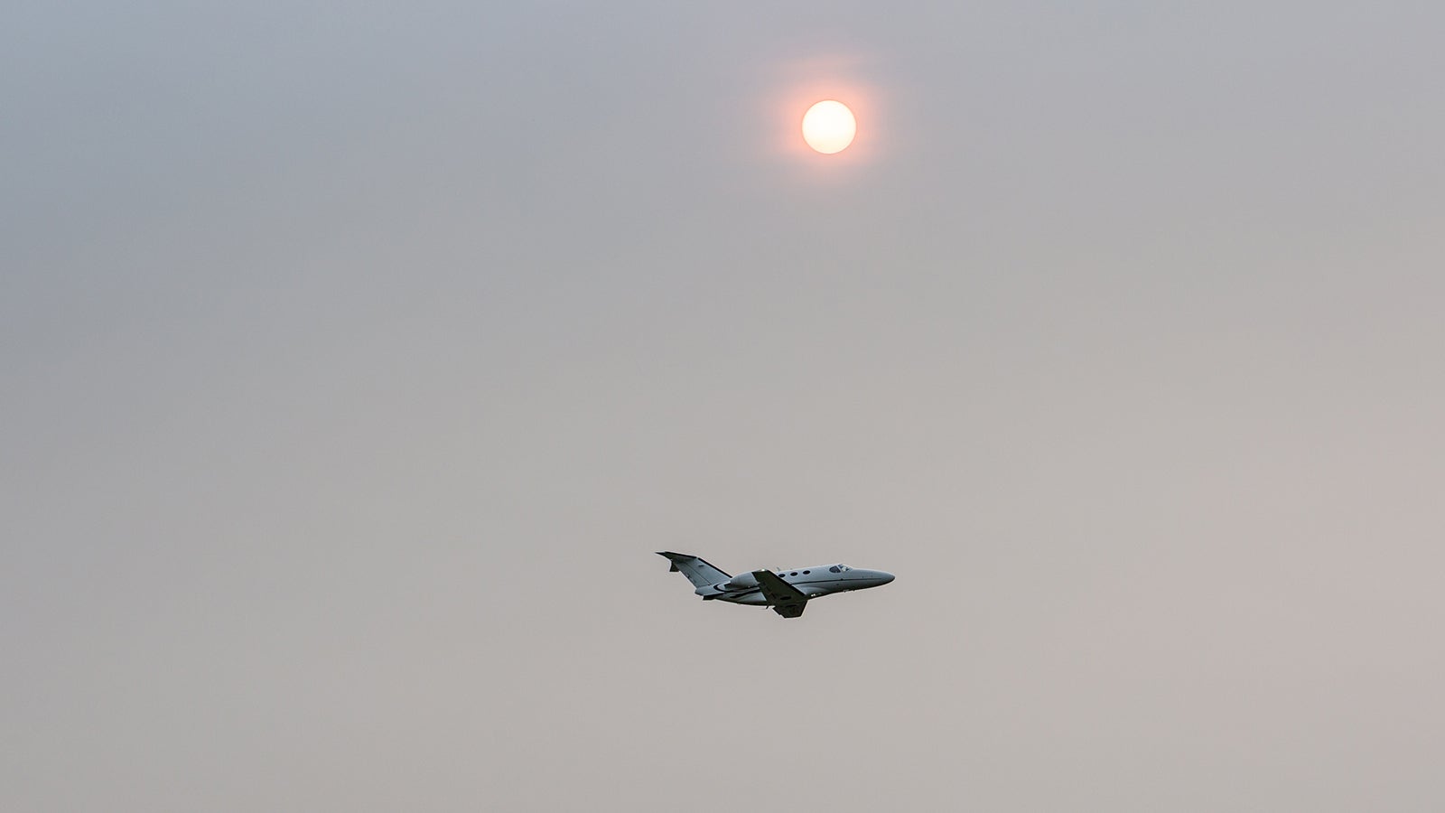 Flugzeug fliegt unter der Sonne, die durch Saharastaub r&ouml;tlich erscheint. 