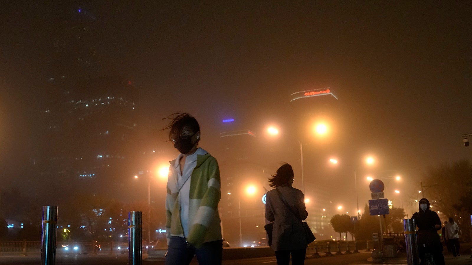 10.04.2023, China, Peking: Menschen mit Gesichtsmasken gehen auf einer Stra&szlig;e durch einen Staub- und Sandsturm. Der Sturm lie&szlig; die Luftqualit&auml;tsindizes in Chinas Hauptstadt in die H&ouml;he schnellen. Foto: Andy Wong/AP/dpa +++ dpa-Bildfunk +++