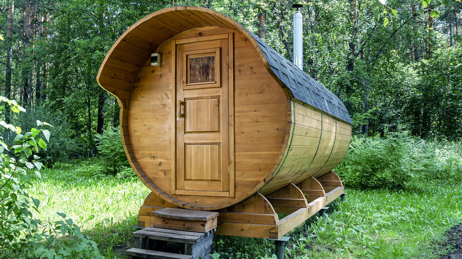 Round wooden barrel bath stands in the forest on a sunny summer day