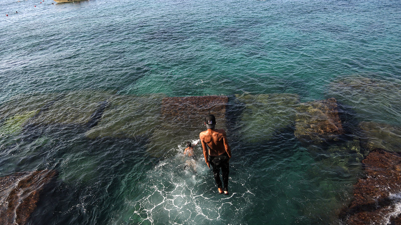 15.08.2025, Libanon, Beirut: Jugendliche erfrischen sich bei den hohen Temperaturen im August an einem &ouml;ffentlichen Strand im Manara-Viertel in Beirut. Im Libanon zeigt sich im Sommer ein krasses Gef&auml;lle: Die Wohlhabenden sonnen sich in exklusiven Strandclubs, w&auml;hrend den weniger Wohlhabenden nur wenige, oft verschmutzte &ouml;ffentliche Str&auml;nde zur Verf&uuml;gung stehen. Trotz der Gesetze, die den &ouml;ffentlichen Zugang vorschreiben, machen hohe Geb&uuml;hren und privatisierte Resorts viele Str&auml;nde f&uuml;r die meisten unerreichbar. (zu dpa: &laquo;Teure Eintrittspreise: Im Libanon sind Strandbesuche Luxus&raquo;) Foto: Marwan Naamani/dpa +++ dpa-Bildfunk +++
