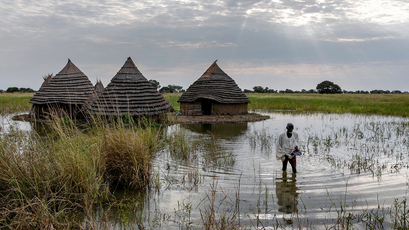 Ein Mann watet durch das Hochwasser auf seinem Grundst&uuml;ck in einem s&uuml;dsudanesischen Dorf. Nachdem der S&uuml;dsudan bereits 2021 schwere &Uuml;berschwemmungen in der Regenzeit erlitt, werden in der nun einsetzenden Regenzeit die schwersten Fluten seit Jahrzehnten erwartet.  Foto: Adrienne Surprenant/AP/dpa 
