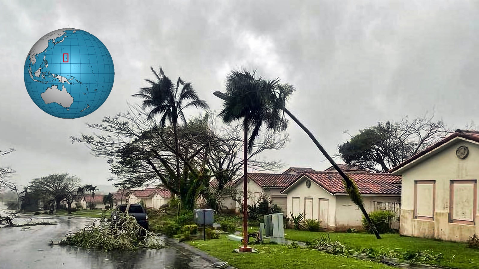 Mehrere besch&auml;digte Palmen und umgest&uuml;rzte &Auml;ste vor H&auml;usern in einer st&uuml;rmischen Wohnsiedlung, oben links eine Weltkugel mit rotem Rechteck.