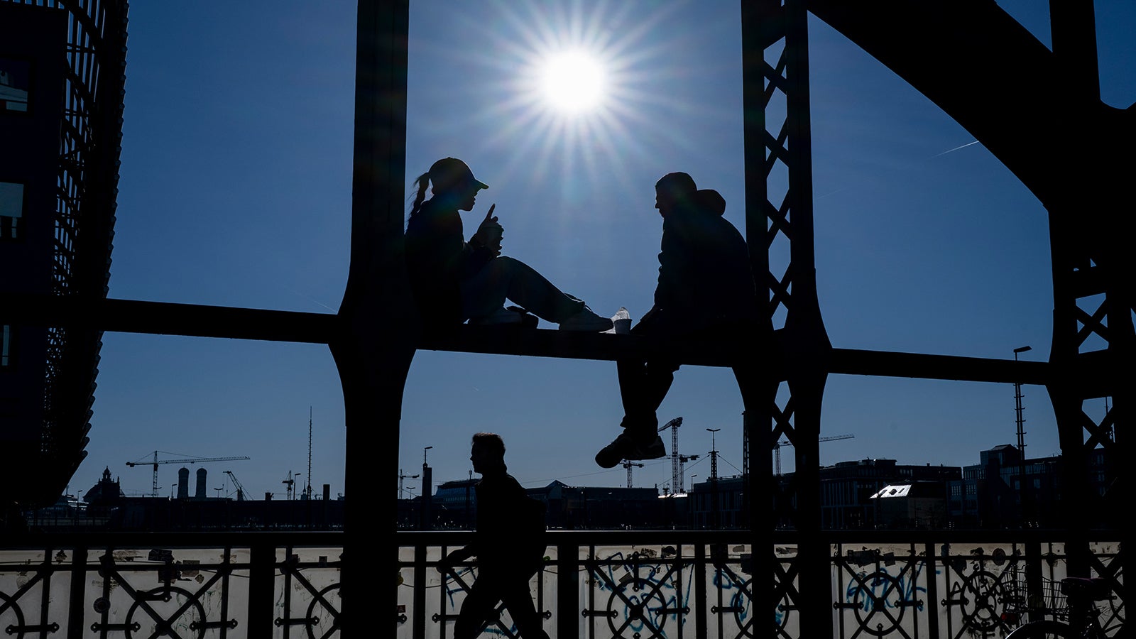 ARCHIV - 13.03.2026, Bayern, M&uuml;nchen: Ein P&auml;rchen sitzt in den Morgenstunden bei strahlend blauen Himmel auf dem Gel&auml;nder der Hackerbr&uuml;cke in der bayerischen Landeshauptstadt. Foto: Peter Kneffel/dpa 