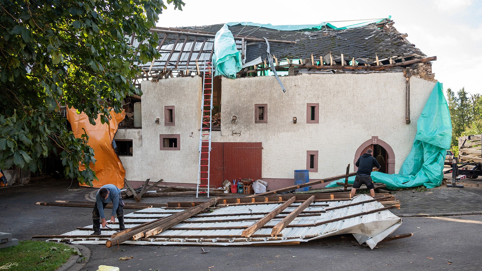 ARCHIV - 22.09.2023, Rheinland-Pfalz, Nusbaum: Zimmerm&auml;nner arbeiten an den Dachtr&uuml;mmern eines Wirtschaftsgeb&auml;ude, das am Vortag von einer Windhose besch&auml;digt wurde. Die Windhose hatte im Eifelkreis zufolge im Ort Nusbaum-Freilingen zahlreiche D&auml;cher abgedeckt. (zu dpa &laquo;Munich Re: 250 Milliarden Dollar Schaden durch Naturkatastrophen&raquo;) Foto: Harald Tittel/dpa +++ dpa-Bildfunk +++