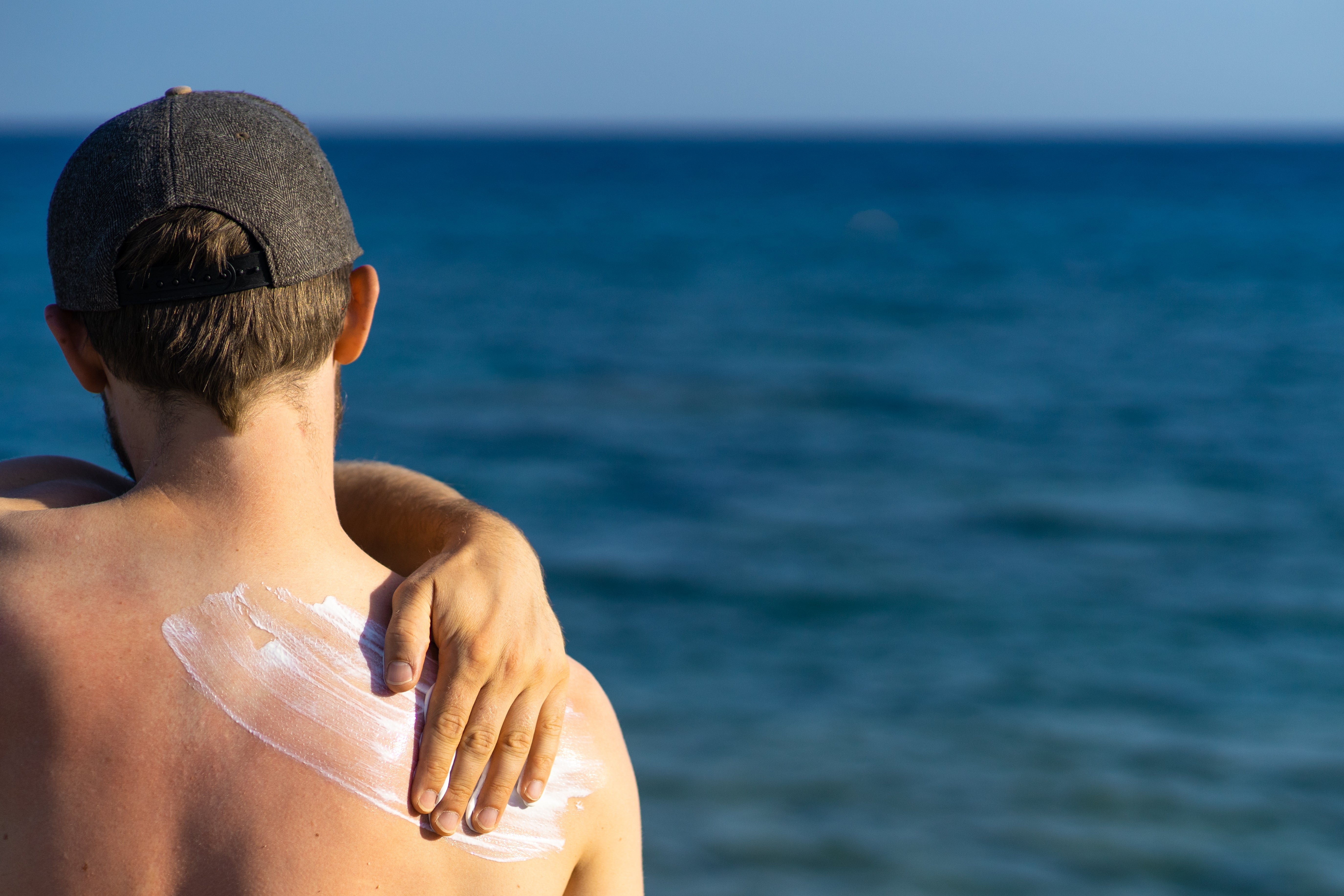 A man coats his shoulder with sunscreen while looking out into the ocean. (Frederik L&ouml;wer / EyeEm / Getty Images)