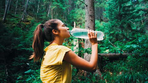 A young woman sips from a water bottle while hiking. It’s important to hydrate while hiking or traveling, especially when it’s hot out. (Mensent Photography via Getty Images)