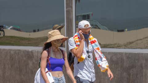 A couple wearing face masks walk in the boardwalk with the beach reflected in a glass window amid the severe heat wave in Venice, Calif., on Aug. 15, 2020. The worst heat wave in several years caused rolling blackouts Aug. 14, 2020, due to power shortages and is setting up dangerous conditions across California. (Apu Gomes/AFP via Getty Images)