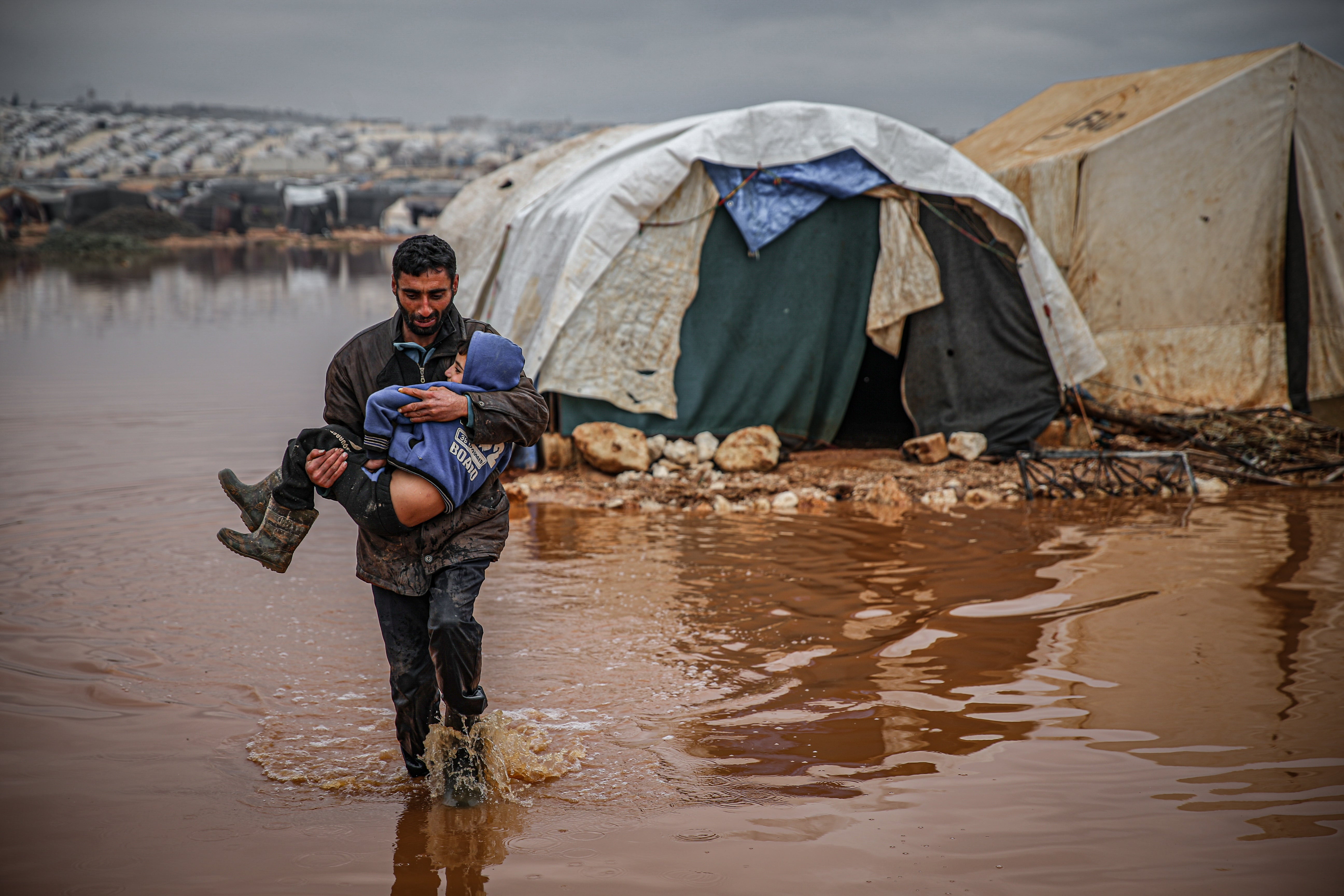 A Syrian civilian carries a child as they evacuate their belongings from flooded tents at the Kefer Lusin refugee camp after heavy rain caused floods in Idlib, Syria on Jan. 19, 2021. Civilians, who fled the attacks of Assad Regime and its supporters in northwestern Syria, are now struggling with harsh weather conditions as many refugee camps are flooded. (Muhammed Said/Anadolu Agency via Getty Images)