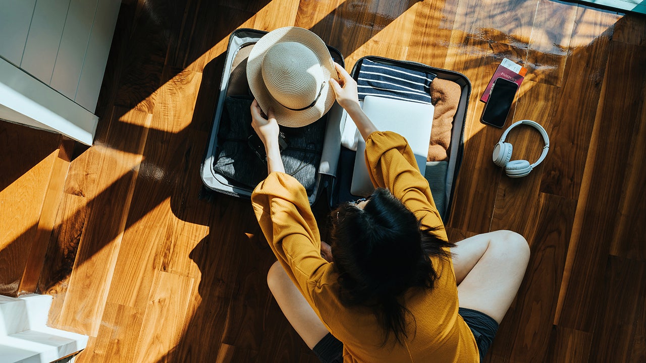 An overhead view shows a woman sitting on the floor in her bedroom, packing a suitcase for a trip. (Getty Images)