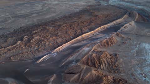 SAN PEDRO DE ATACAMA, CHILE - AUGUST 26: In this aerial view, twilight falls on the Valle de la Luna in the Atacama Desert, considered the driest place on earth on August 26, 2022 near San Pedro de Atacama, Chile. Much of the desert receives less than half an inch of rainfall per year and some areas none at all for hundreds of years. Located in Chile's northern third between two mountain ranges, the Atacama is possibly the oldest desert on earth, experiencing extreme aridity for at least 3 million years. The extreme aridity makes it one of the clearest places on earth to view the night sky, and is home to the largest radio telescope in the world, the Atacama Large Millimeter/submillimeter Array (ALMA) telescope. The Valley of the Moon is so called because of its lunar and even Mars-like appearance. (Photo by John Moore/Getty Images,)