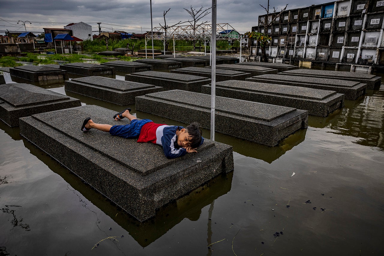 A boy lies on top of a tomb at a flooded cemetery following Tropical Storm Nalgae, as Filipinos mark All Saints' Day on Nov. 1, 2022, in Masantol, Pampanga Province, Philippines. Millions of Filipinos flock to cemeteries around the country to visit departed loved ones on All Saints' Day, a holiday celebrated in Catholic cultures around the world during which family and friends of the deceased gather at cemeteries to pray and hold vigils for those who have passed away. (Ezra Acayan/Getty Images)