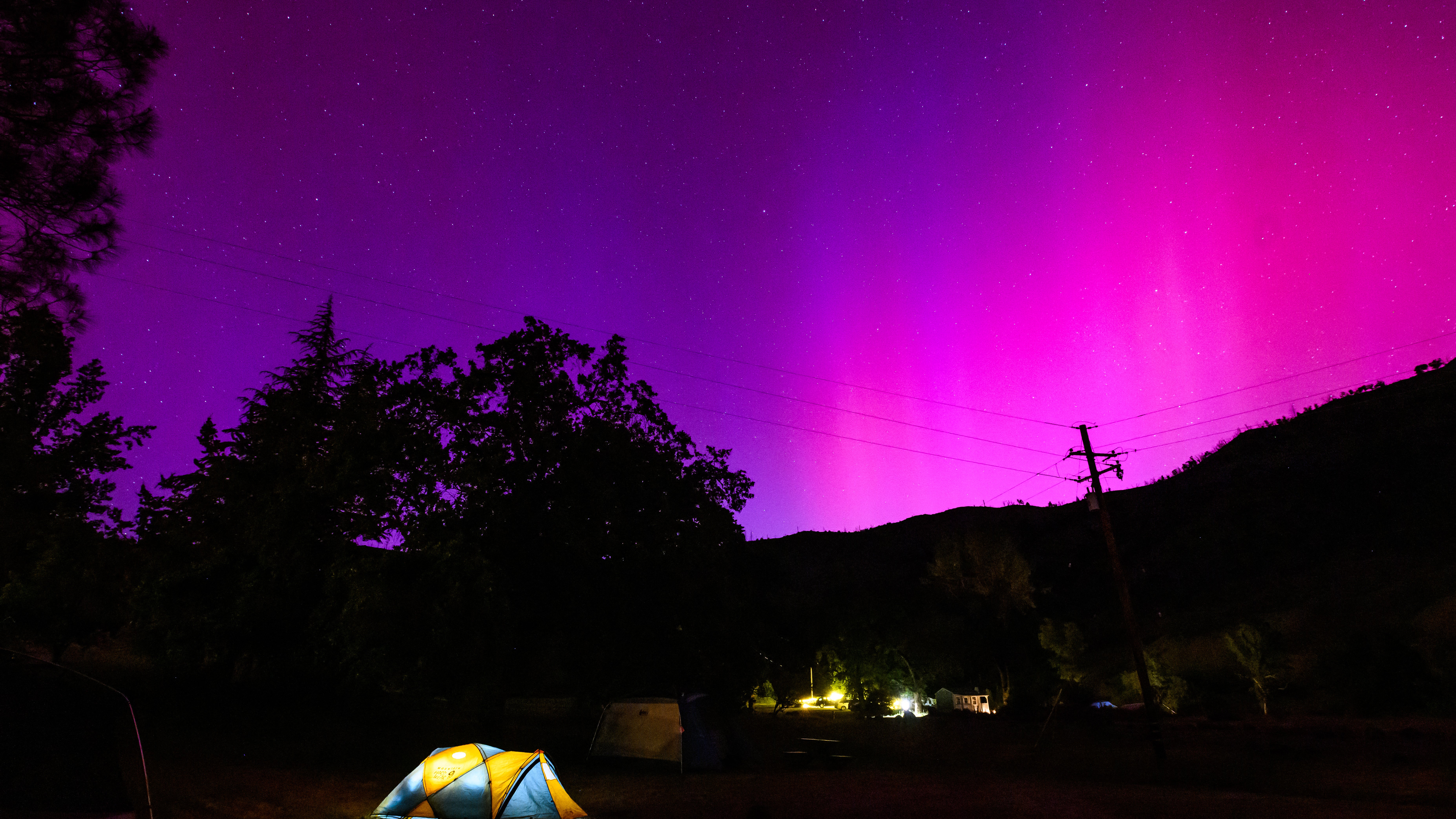 TOPSHOT - Northern lights or aurora borealis illuminate the night sky over a camper's tent north of San Francisco in Middletown, California on May 11, 2024. The most powerful solar storm in more than two decades struck Earth, triggering spectacular celestial light shows from Tasmania to Britain -- and threatening possible disruptions to satellites and power grids as it persists into the weekend. (Photo by JOSH EDELSON / AFP) (Photo by JOSH EDELSON/AFP via Getty Images)