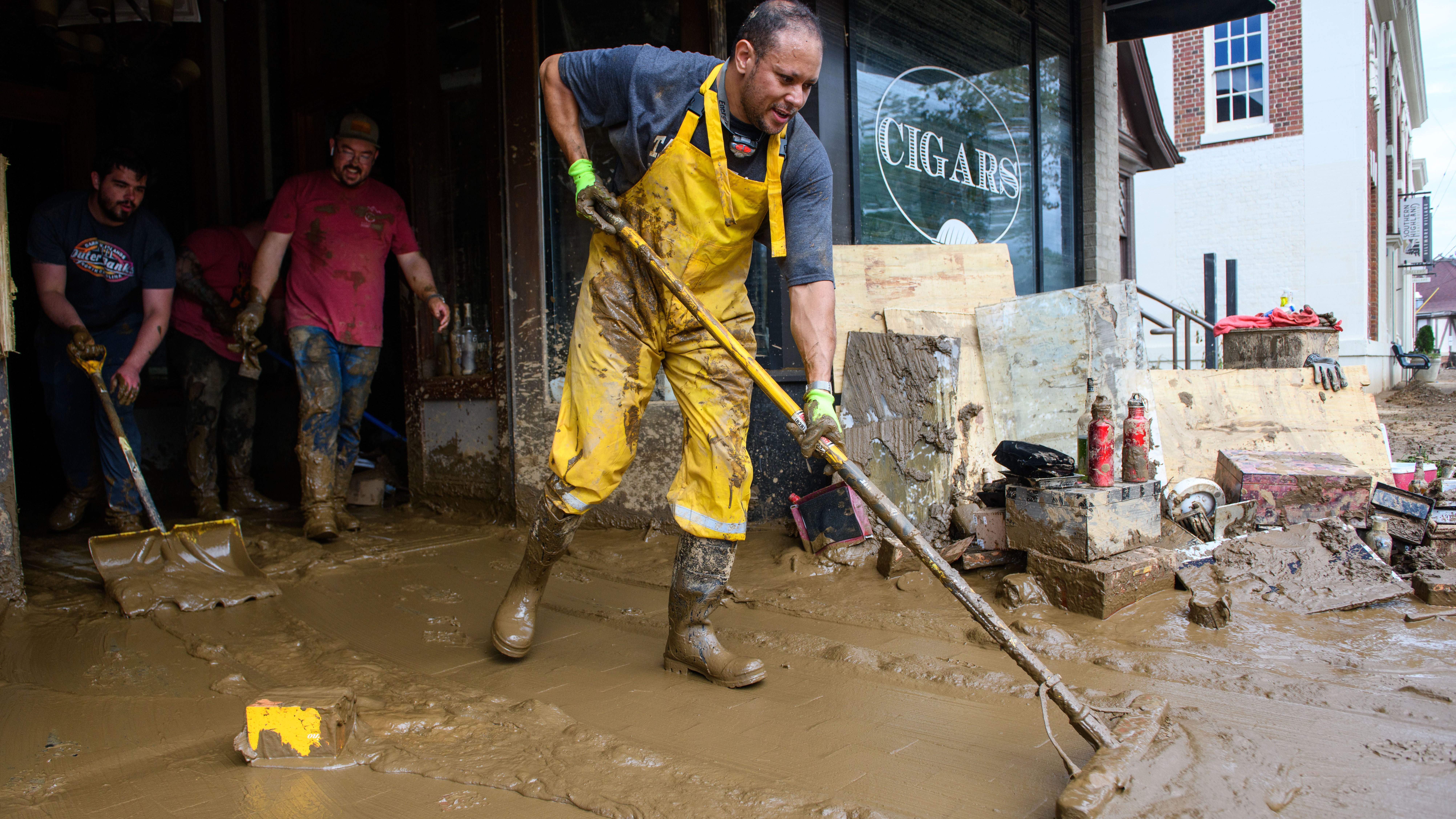 ASHEVILLE, NORTH CAROLINA - OCTOBER 01: Sam Souhail, far right, owner of the Casablanca Cigar Bar, clears mud from his shop at the Biltmore Village across from the Biltmore Estate in the aftermath of Hurricane Helene on October 1, 2024 in Asheville, North Carolina. According to reports, at least 140 people have been killed across the southeastern U.S., and millions are without power due to the storm, which made landfall as a Category 4 hurricane. The White House has approved disaster declarations in North Carolina, Florida, South Carolina, Tennessee, Georgia, Virginia and Alabama, freeing up federal emergency management money and resources for those states. (Photo by Melissa Sue Gerrits/Getty Images)
