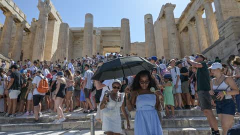 Tourists wear hats and carry umbrellas for protection as they visit the Acropolis during the worst heatwave of the season in Athens, Greece, on July 22, 2025. The Acropolis shuts between 12:00 and 17:00 to protect visitors and workers from the intense heat. (Photo by Nicolas Koutsokostas/NurPhoto via Getty Images)