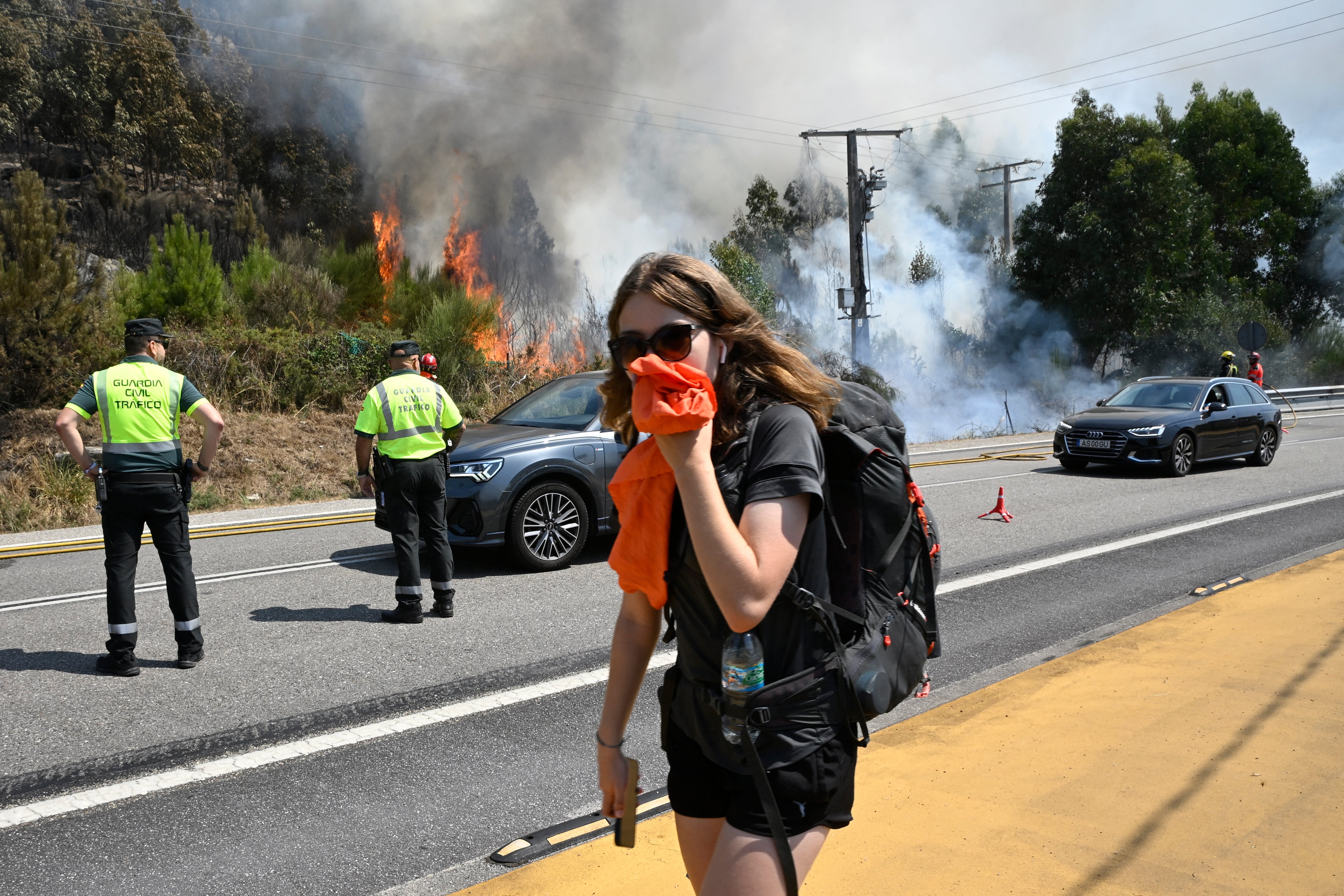 TOPSHOT - A pilgrim on her way to Santiago de Compostela covers her mouth as she walks past a wildfire near the village of Mougas, in Oia municipality, northwestern Spain on August 22, 2025. The northwestern regions of Galicia and Castile and Leon, along with Extremadura in the west, have been hit hardest by the fires raging since early August in the scorching heat. More than 403,000 hectares (996,000 acres) have been burnt in Spain this year, according to the European Forest Fire Information System. (Photo by MIGUEL RIOPA / AFP) (Photo by MIGUEL RIOPA/AFP via Getty Images)          