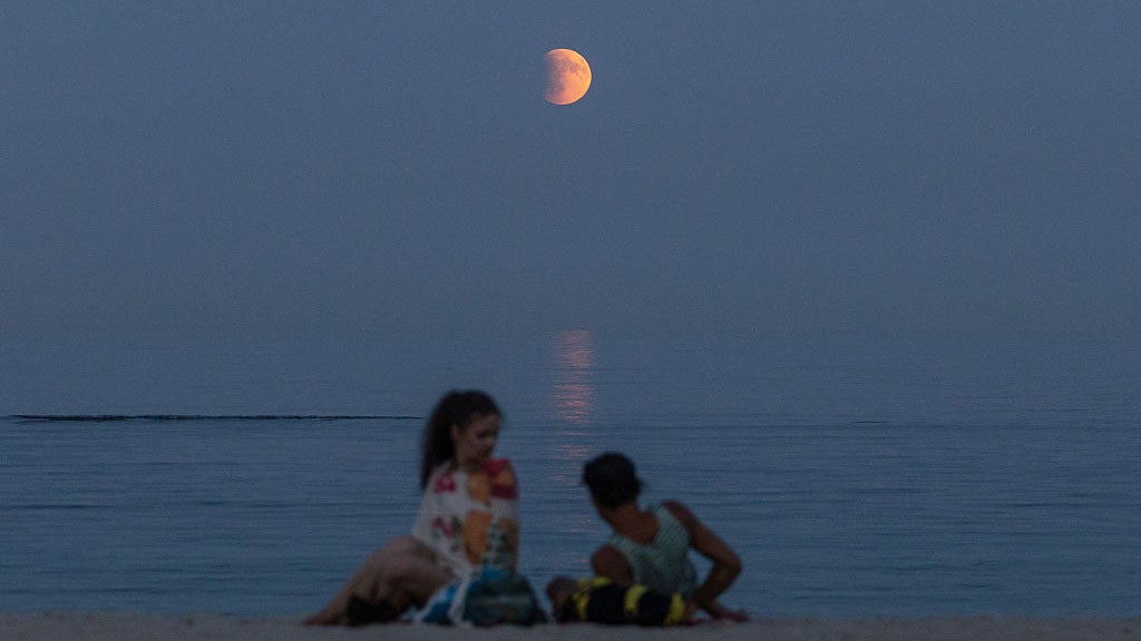 Beach-goers rest on a shore of the Black Sea with a full moon also known as "Blood Moon" during a phase of a total eclipse in the background in Odesa, on September 7, 2025, amid the Russian invasion of Ukraine. Stargazers will have a chance to see a "Blood Moon" on September 7, 2025, night during a total lunar eclipse visible across Asia and swathes of Europe and Africa. (Photo by Oleksandr GIMANOV / AFP) (Photo by OLEKSANDR GIMANOV/AFP via Getty Images)          