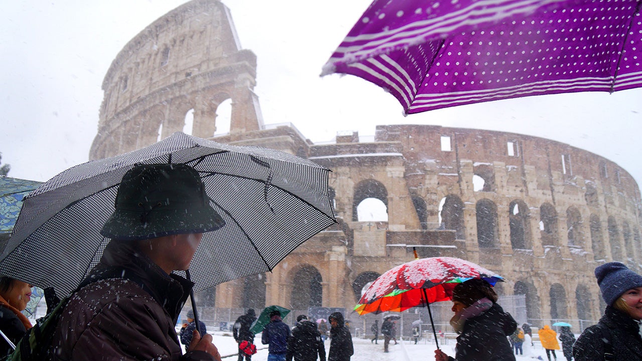 Tourists shed under umbrellas as they visit the ancient Colosseum during a snowfall in Rome on February 26, 2018.  (Vincenzo Pinto/AFP/Getty Images)                                                                