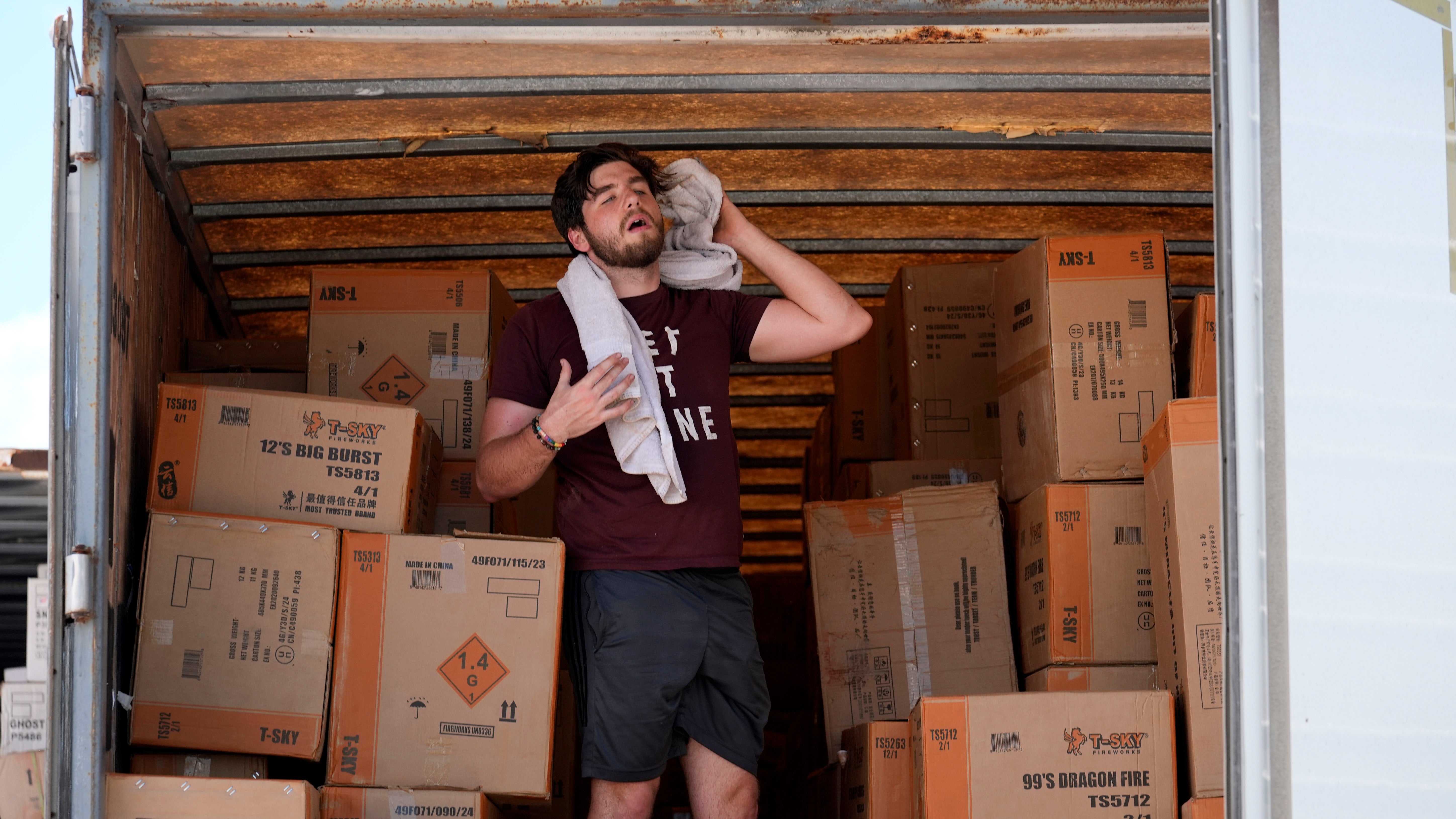 Ethan Hickman uses a towel to wipe off sweat as he takes a break from unloading a stiflingly hot trailer of fireworks outside Powder Monkey Fireworks ahead of the opening of the stand Monday, June 17, 2024, in Weldon Spring, Mo. (AP Photo/Jeff Roberson)